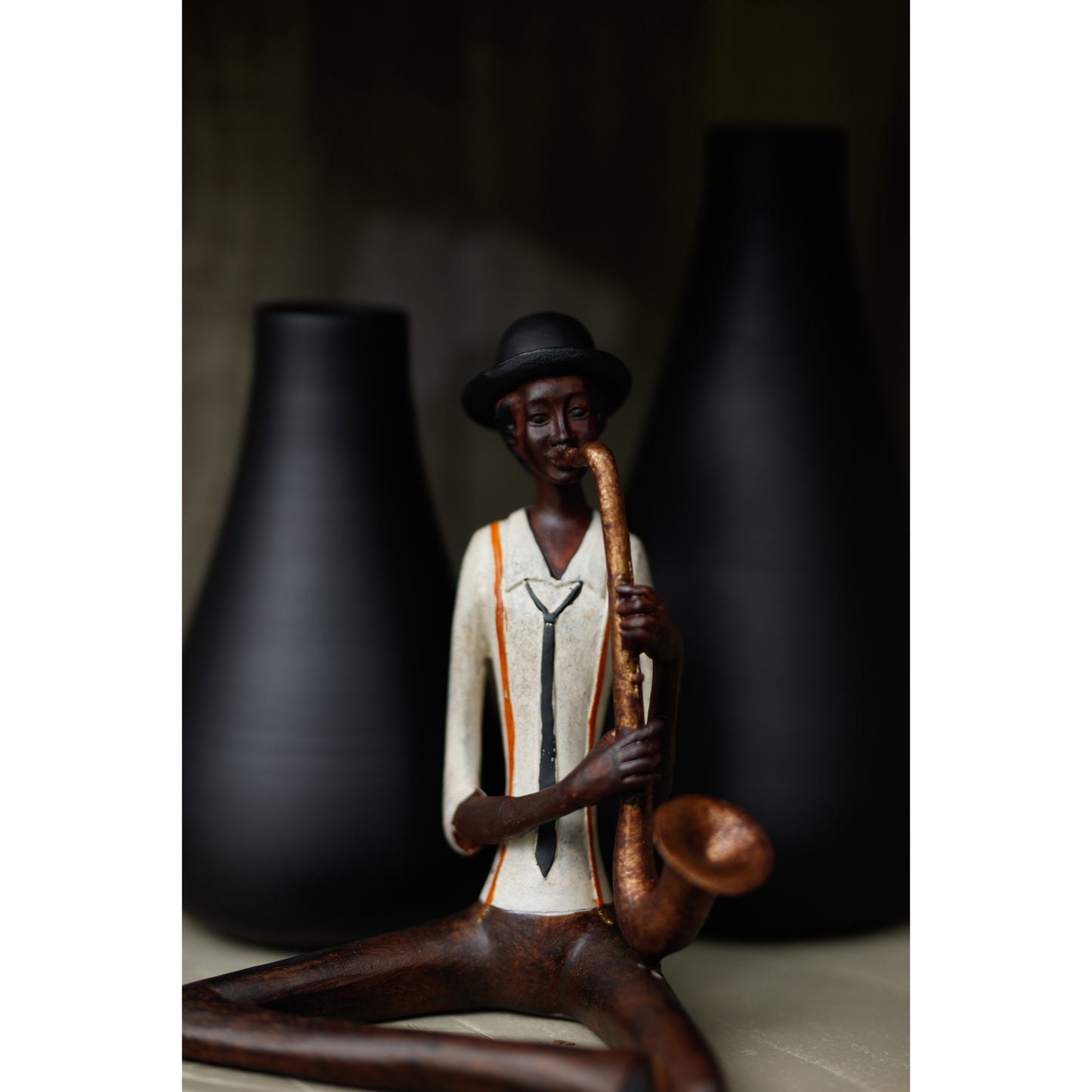 Sitting jazz saxophonist figurine in elegant attire, featuring detailed craftsmanship, against dark vases, exuding musical charm.