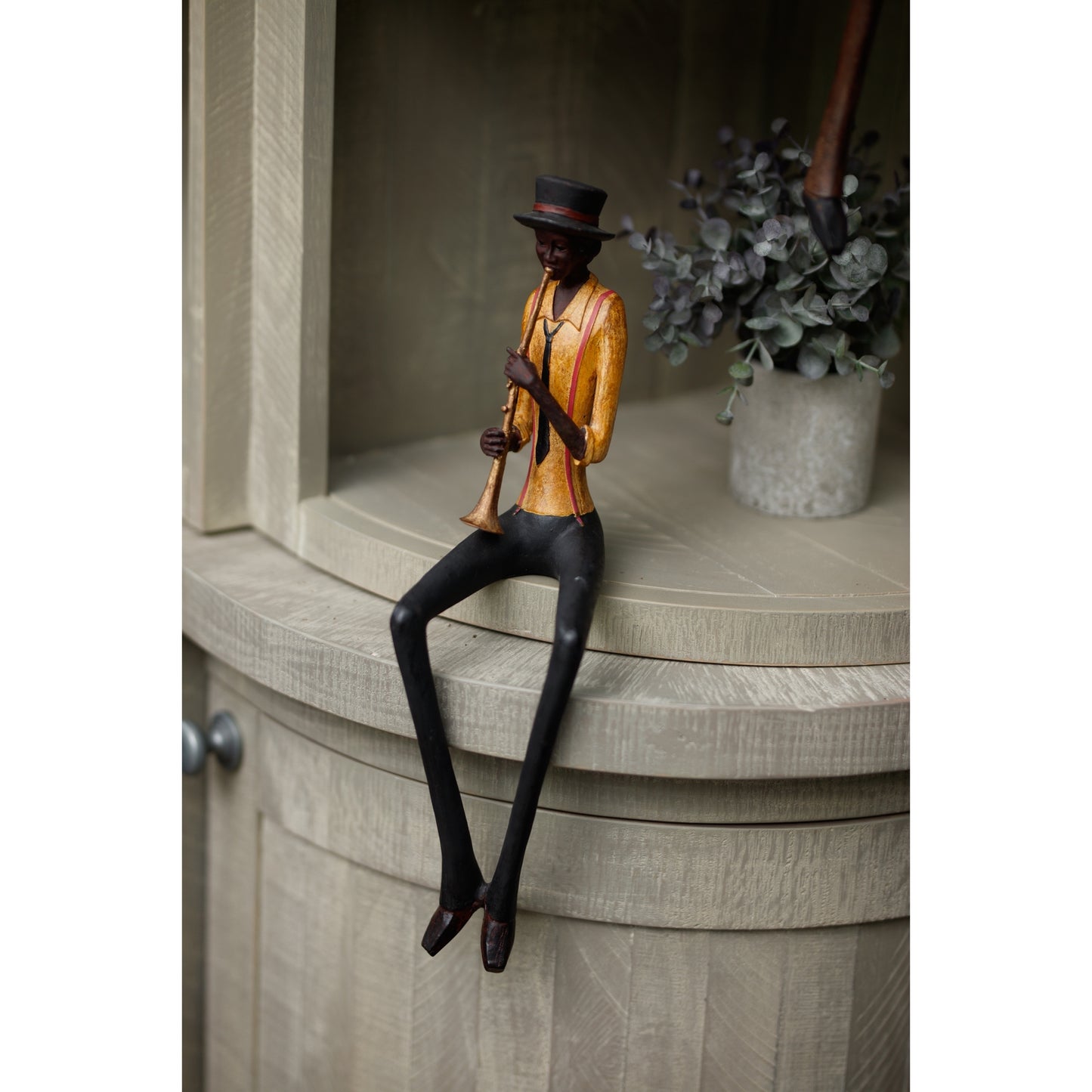 Sitting jazz band trumpeter figurine with elegant details, wearing an orange shirt and black hat, showcased on a wooden shelf.