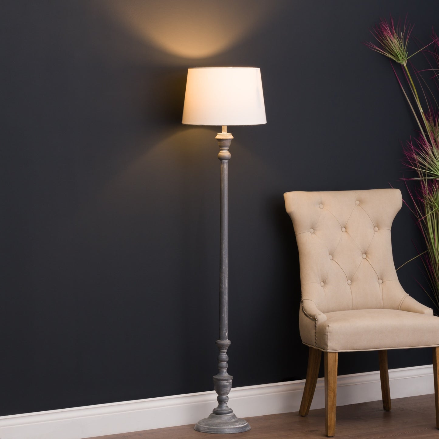 Sophisticated grey floor lamp with a classic linen shade, illuminating a cozy space next to a beige upholstered chair.