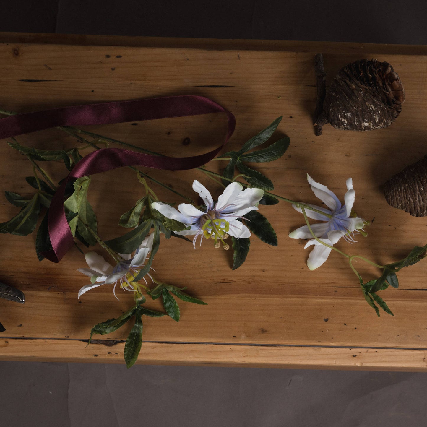 Liflike Passion Flower Spray featuring white petals with delicate purple accents and lush green leaves on a wooden surface.