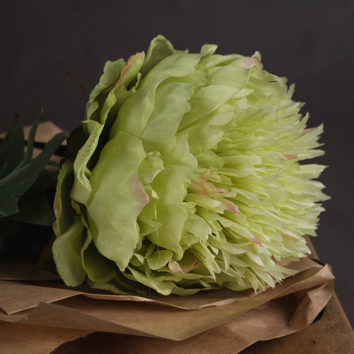 Soft sage-green peony with detailed petals, resting on textured brown paper, exuding elegance for versatile home decor.