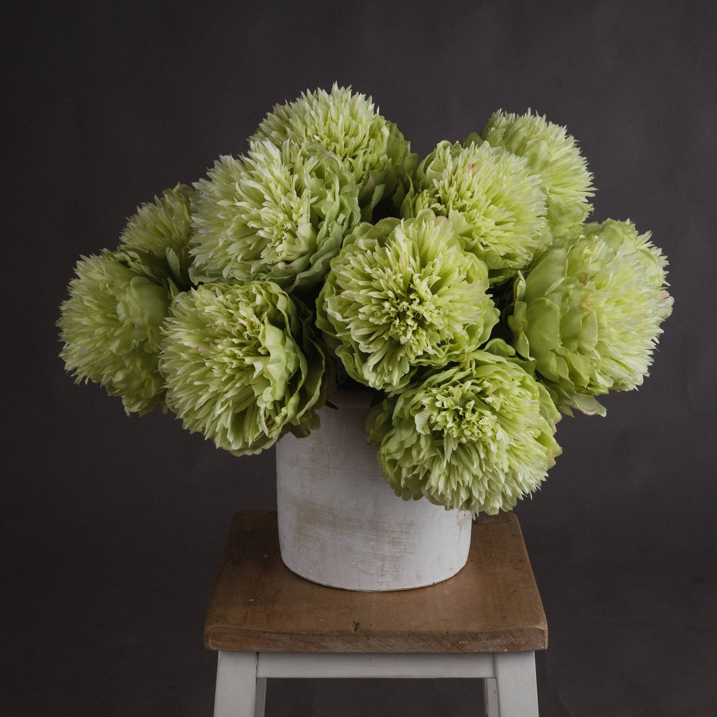 Soft sage-green artificial peonies in a white pot, showcasing full blooms that add elegance and sophistication to decor.