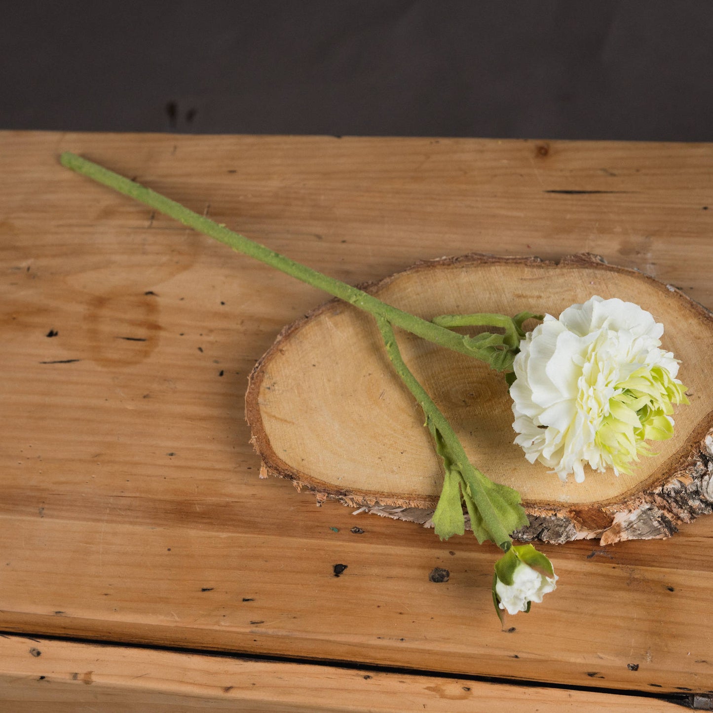Lifelike green ranunculus spray with delicate blooms and a natural stem, resting on a rustic wooden slice. Perfect for home decor.