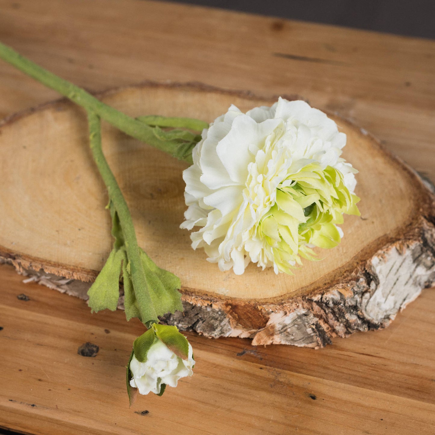 Vibrant green ranunculus spray with lifelike blooms and textured leaves, set on a rustic wood slice background.