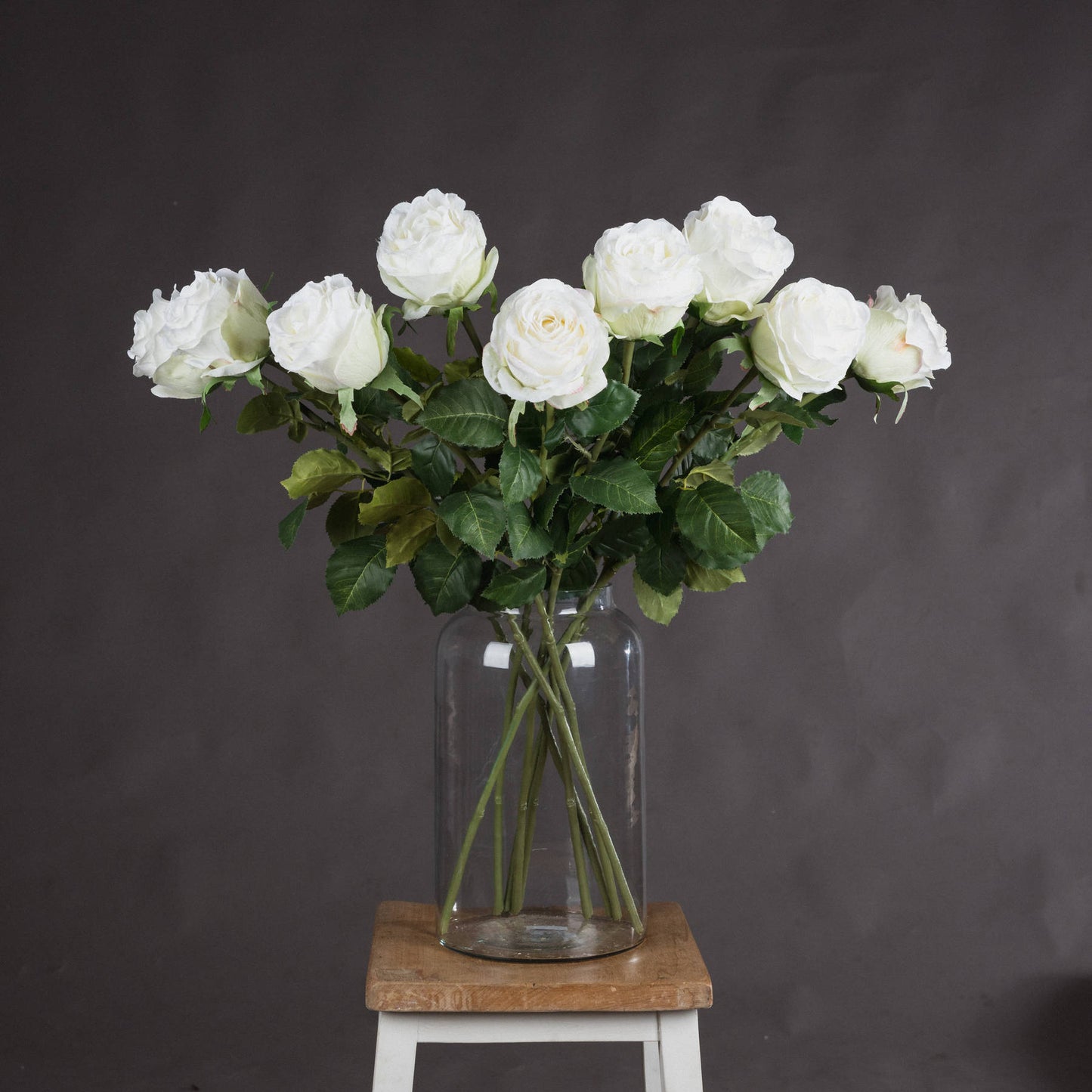 Elegant artificial white roses in a clear vase, featuring lush green leaves, perfect for home decor or centerpieces.