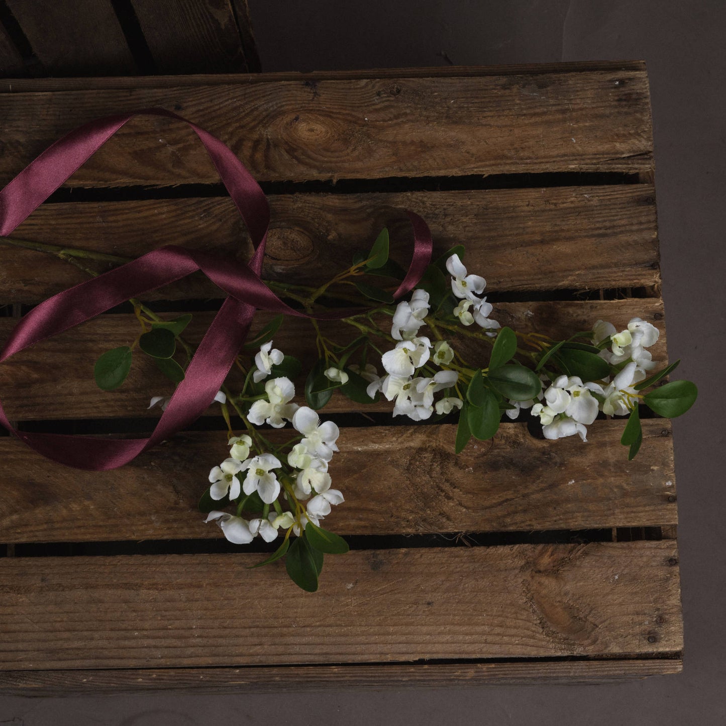 Lifelike white Mock Orange flowers with green leaves, elegantly arranged on a rustic wooden surface with a burgundy ribbon.