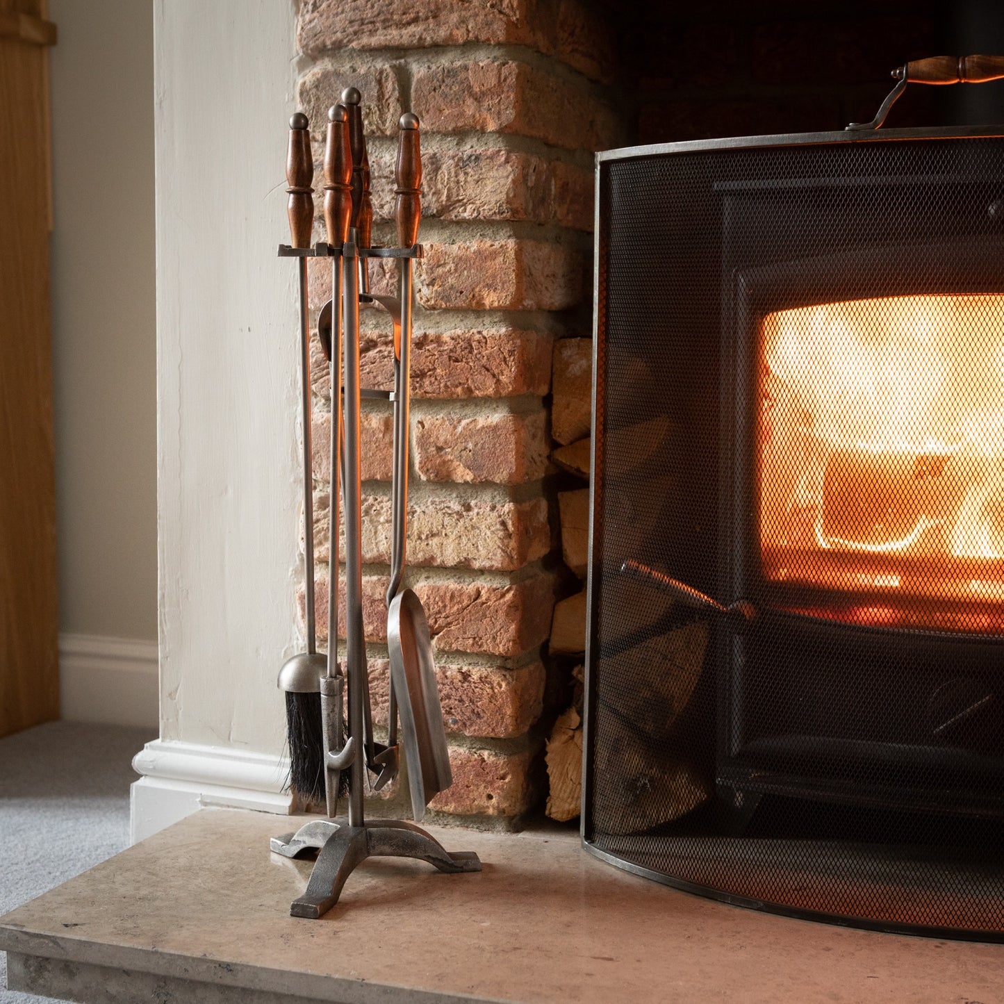 Hand-turned antique pewter fire companion set with wooden handles, showcasing elegant design next to a glowing fireplace.