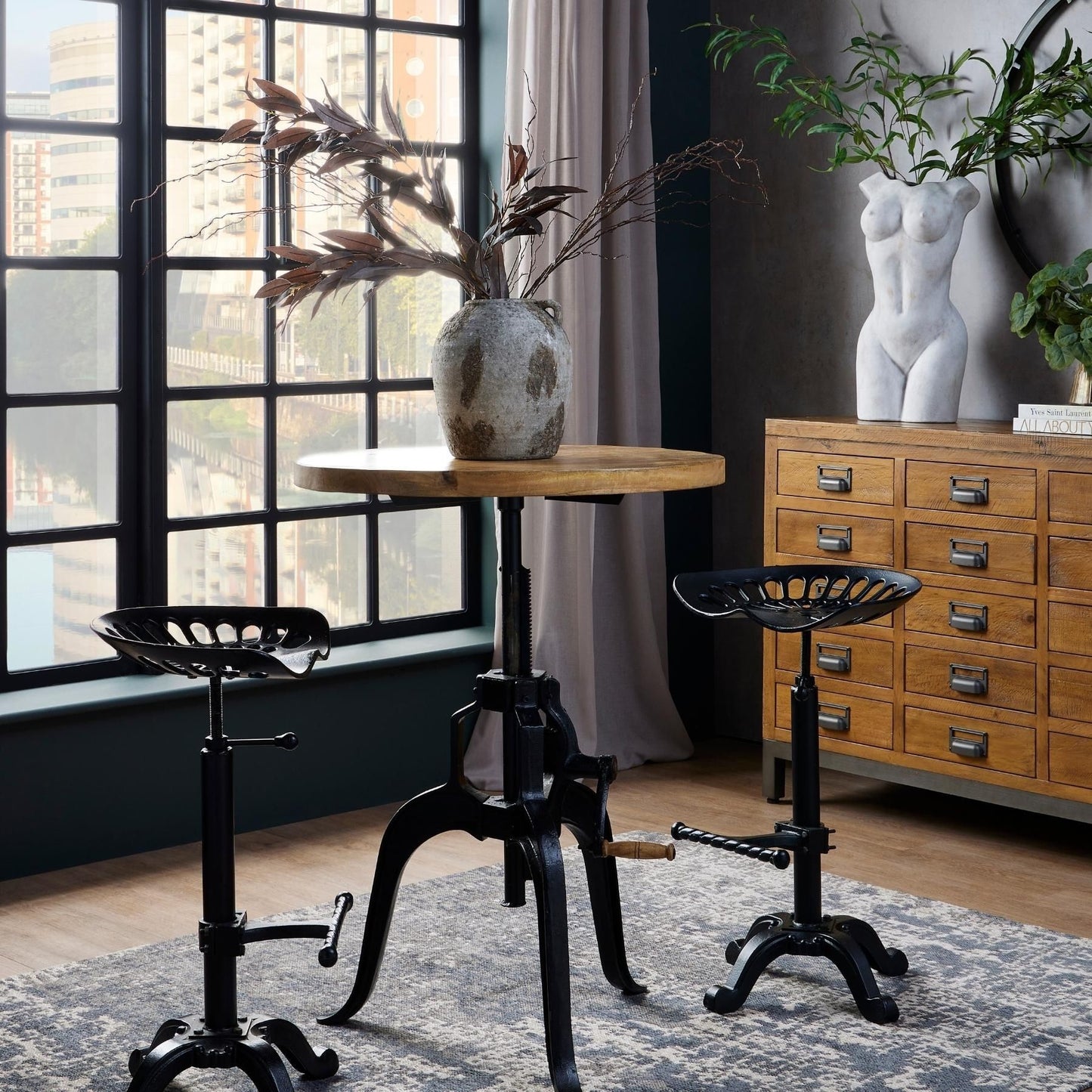 Industrial-style adjustable bar table with a weathered wood top, sturdy black metal frame, and two matching stools in a stylish setting.