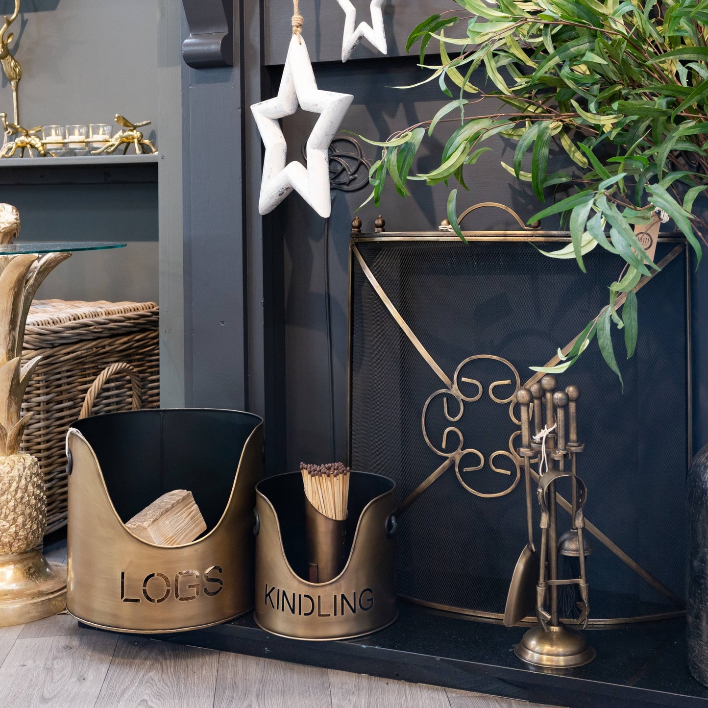 Bronze finish log and kindling buckets with cut-out lettering, paired with a matchstick holder, creating a cozy fireside ambiance.