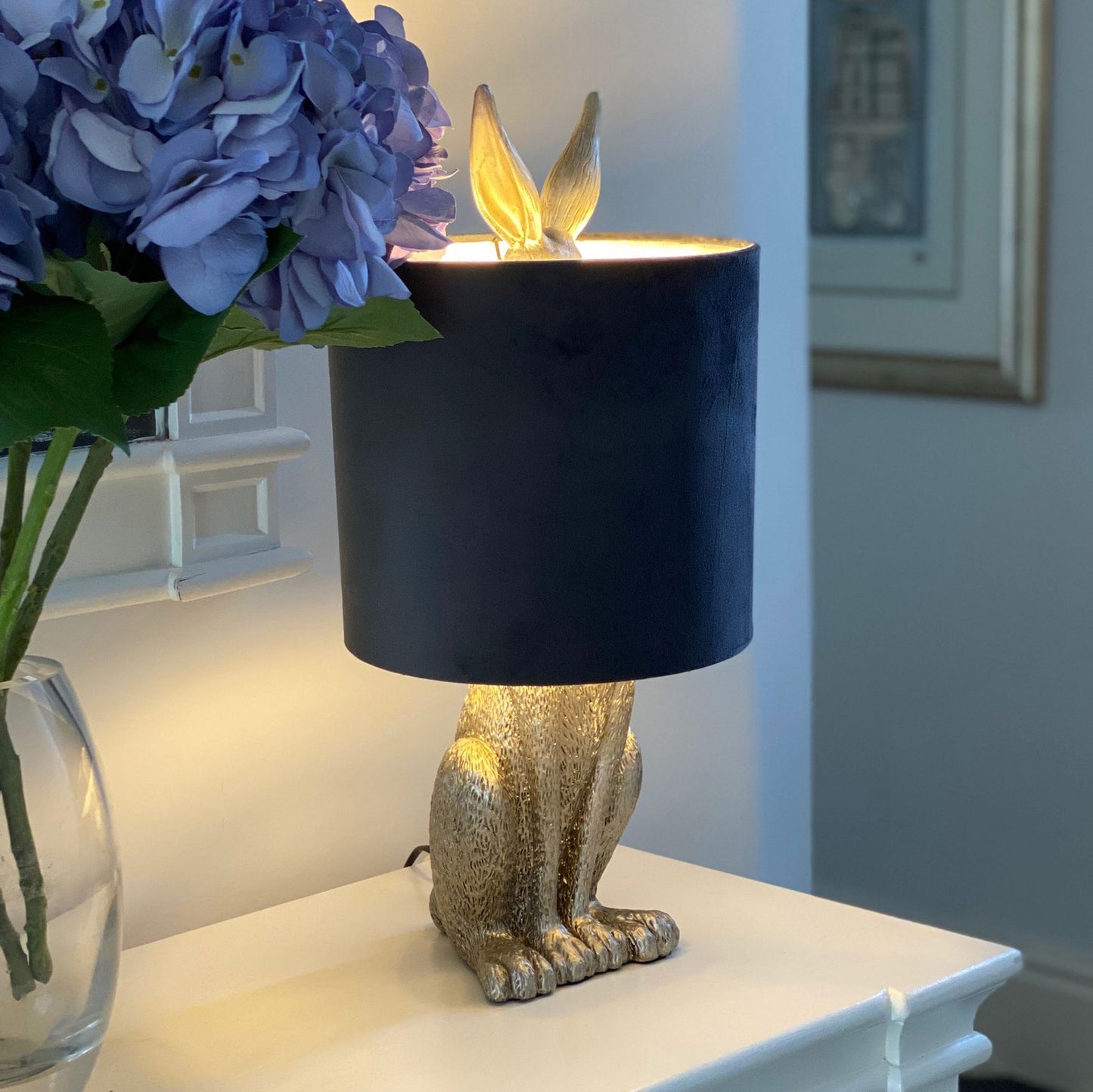 Silver hare table lamp with a luxurious grey velvet shade, featuring playful design and a warm glow, accentuating elegant decor.