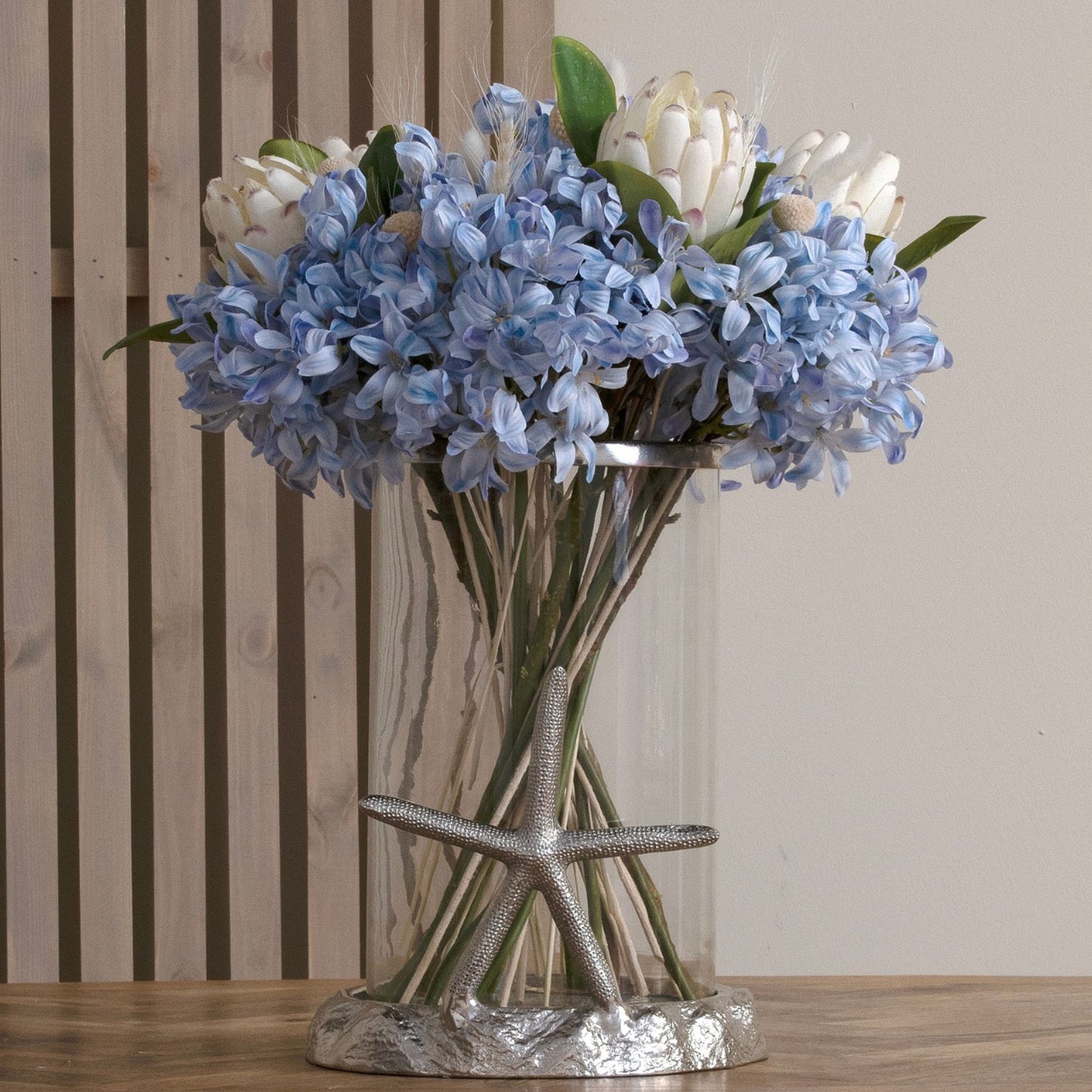 Light blue artificial agapanthus flowers in a clear vase with a silver starfish base, adding a coastal elegance to interiors.