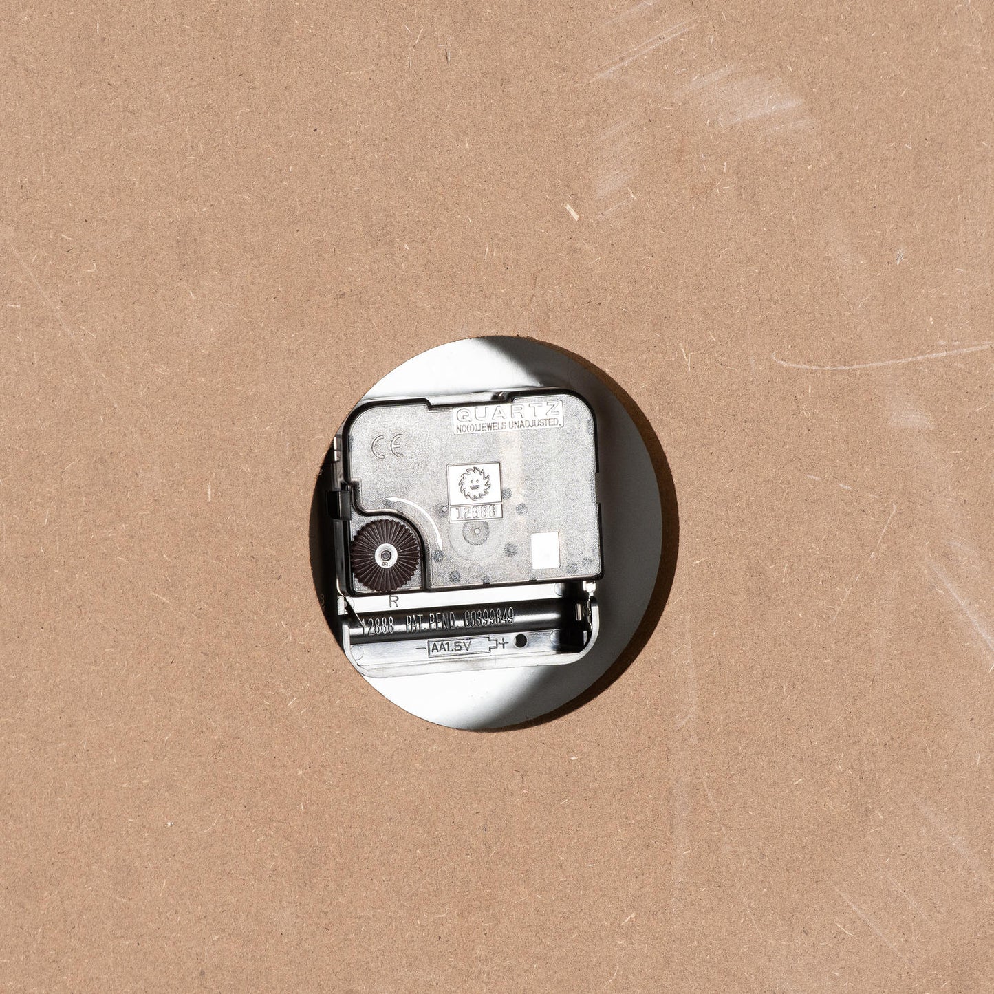 Quartz clock mechanism mounted on a circular cutout, set against a textured brown surface.