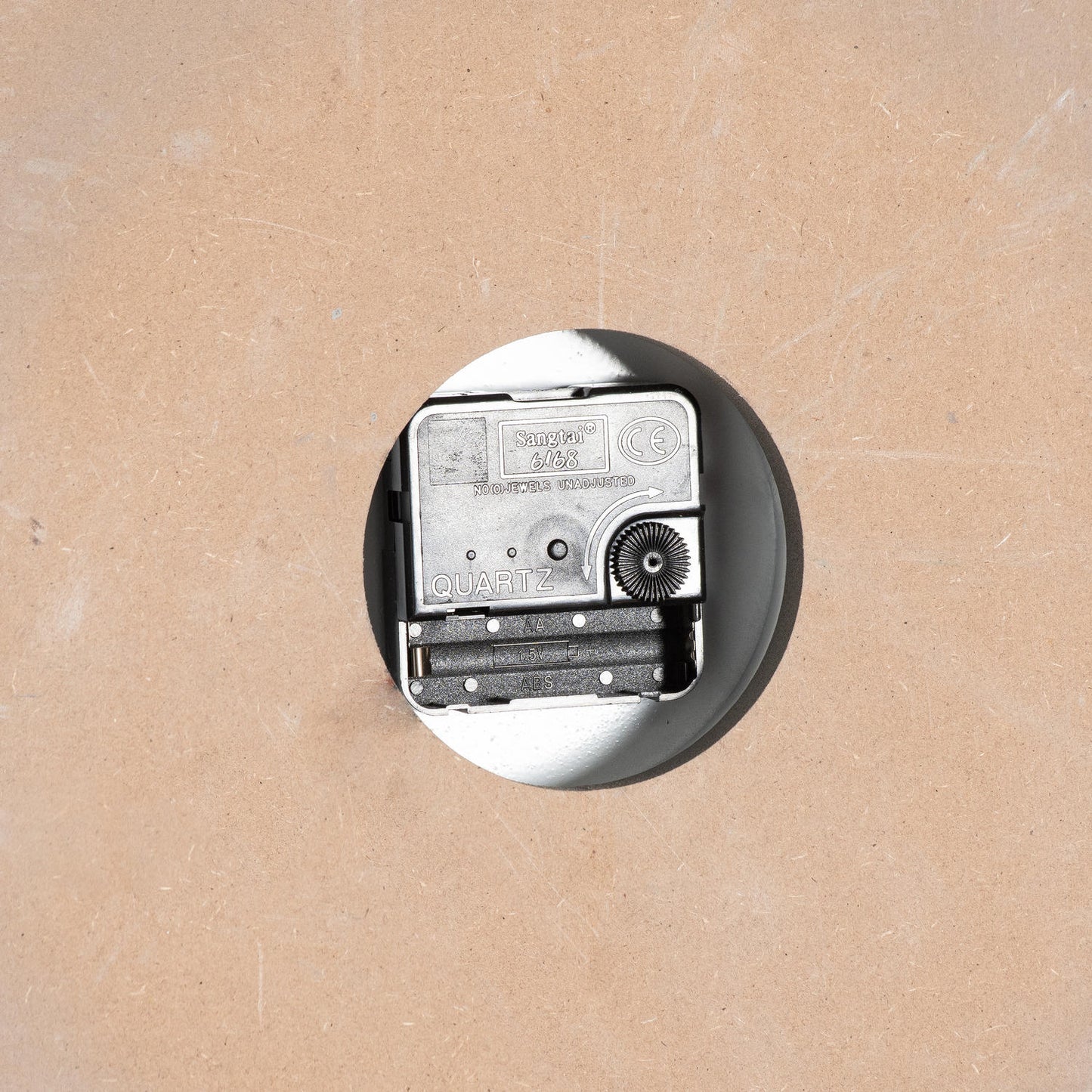 Close-up of a quartz clock mechanism set in a round hole, showcasing the inner workings against a neutral background.
