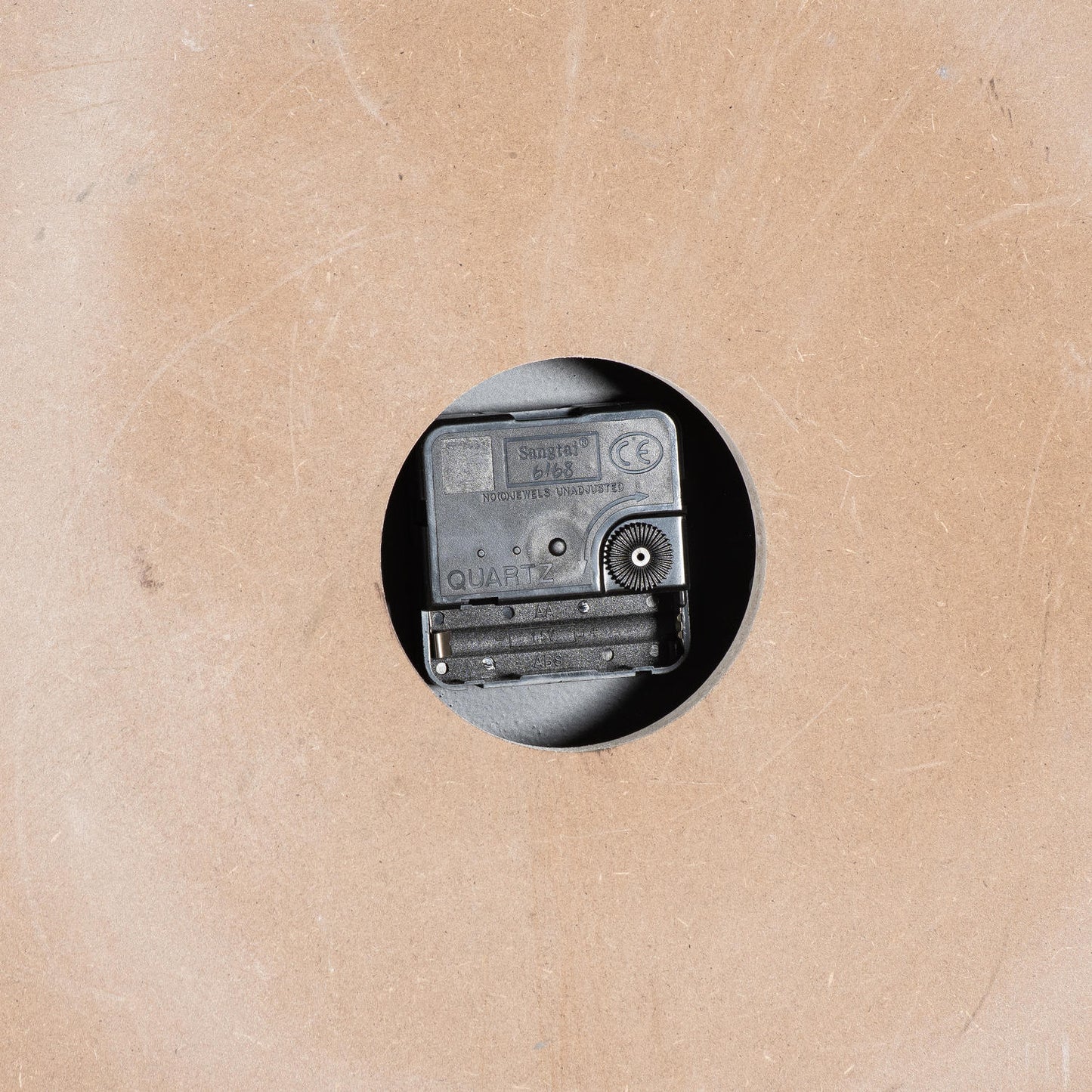 Quartz clock mechanism mounted on a beige backing, featuring a circular cutout for wall display.