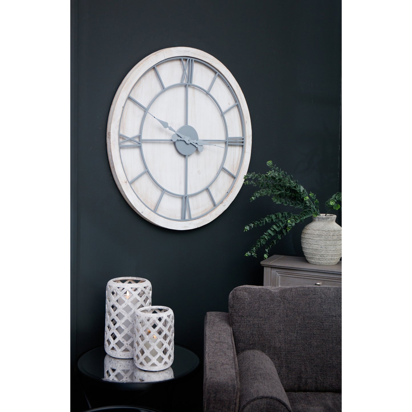 Large white wall clock featuring a round whitewashed wood frame and light grey Roman numerals, mounted on a dark wall.