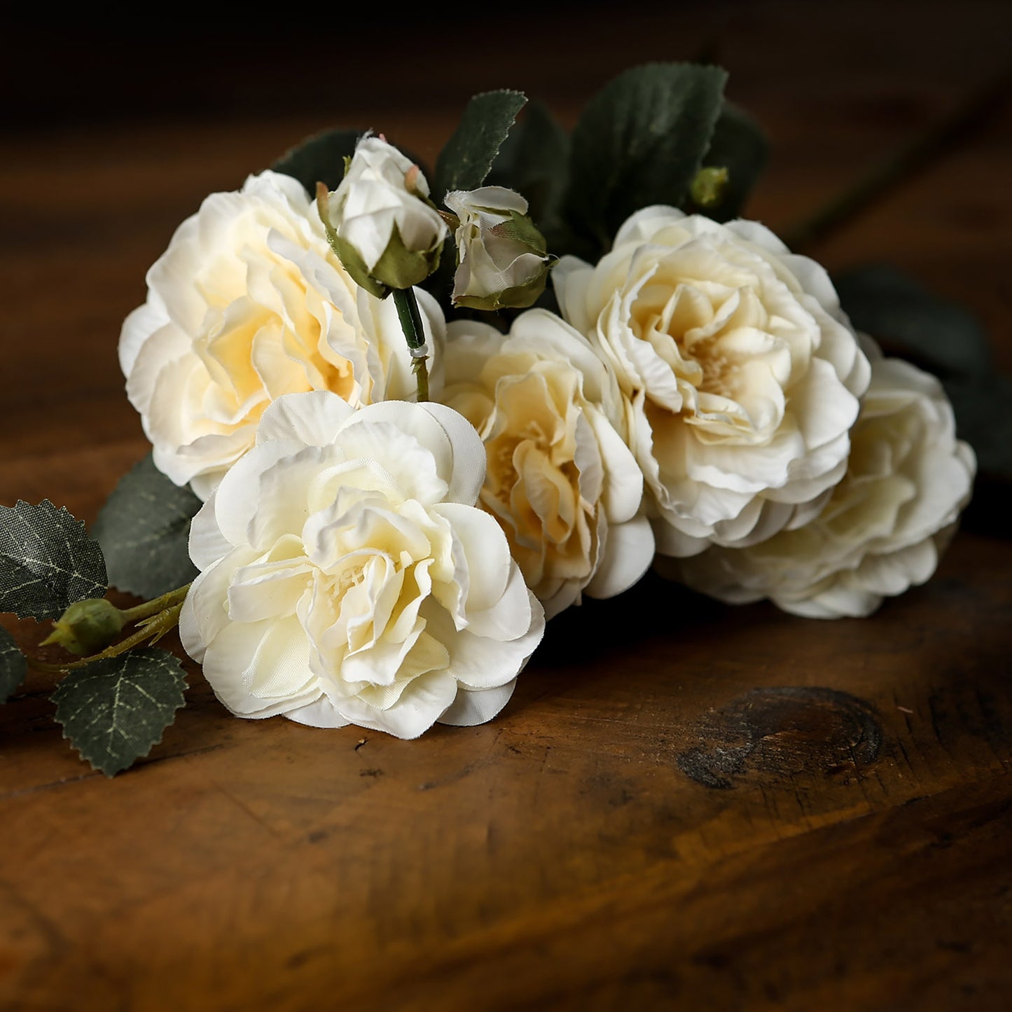 Soft white cottage roses with lush, multi-petaled blooms and green foliage, elegantly arranged on a wooden surface.