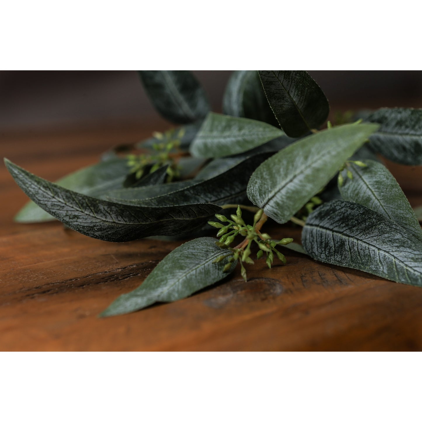 Lifelike green eucalyptus spray with detailed leaves and seed pods, resting on a rustic wooden surface, perfect for decor.