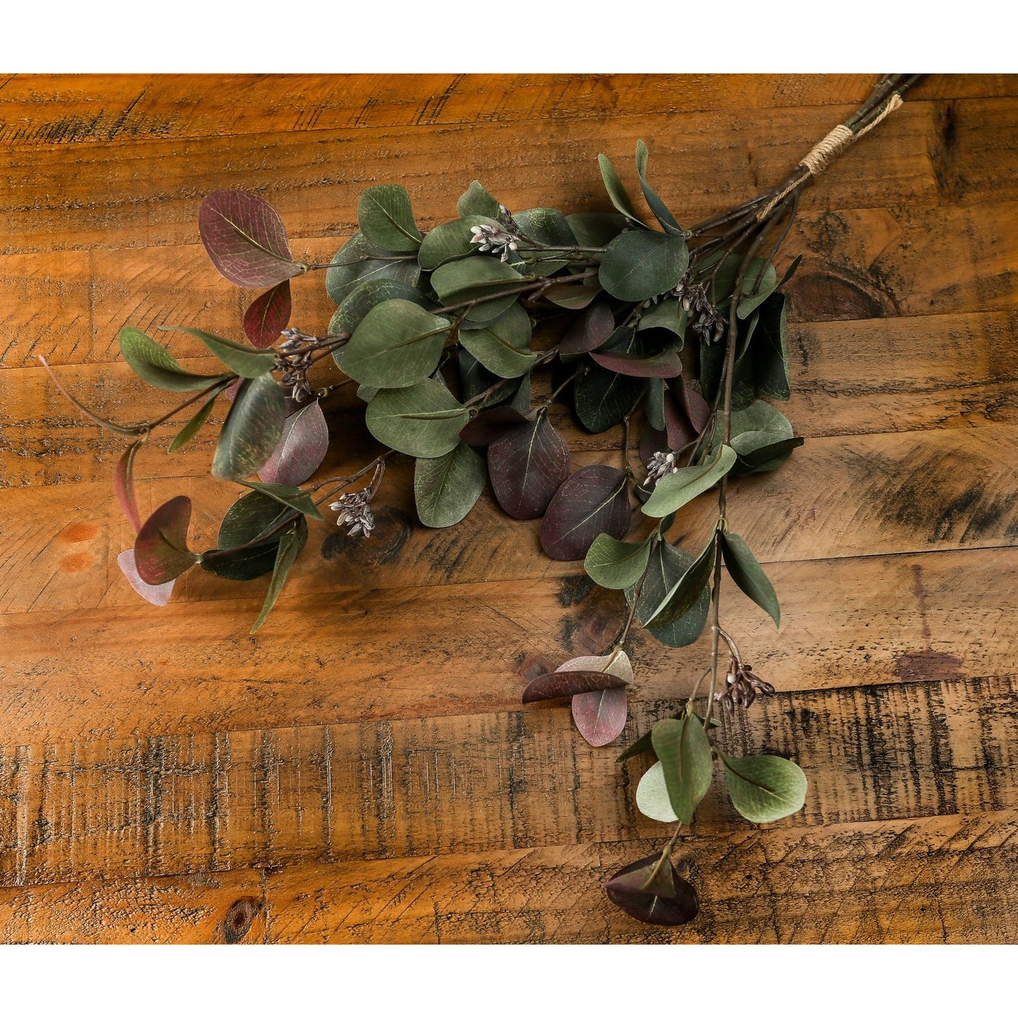 Variegated eucalyptus bouquet featuring sage greens, misty greys, and ruby accents, set against a rustic wooden background.