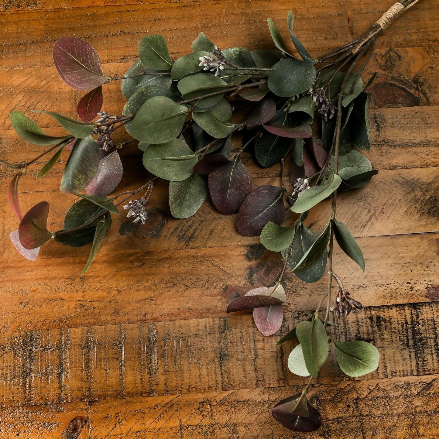 Variegated eucalyptus bouquet with sage green and ruby leaves, elegantly crafted for year-round sophistication on a wooden surface.