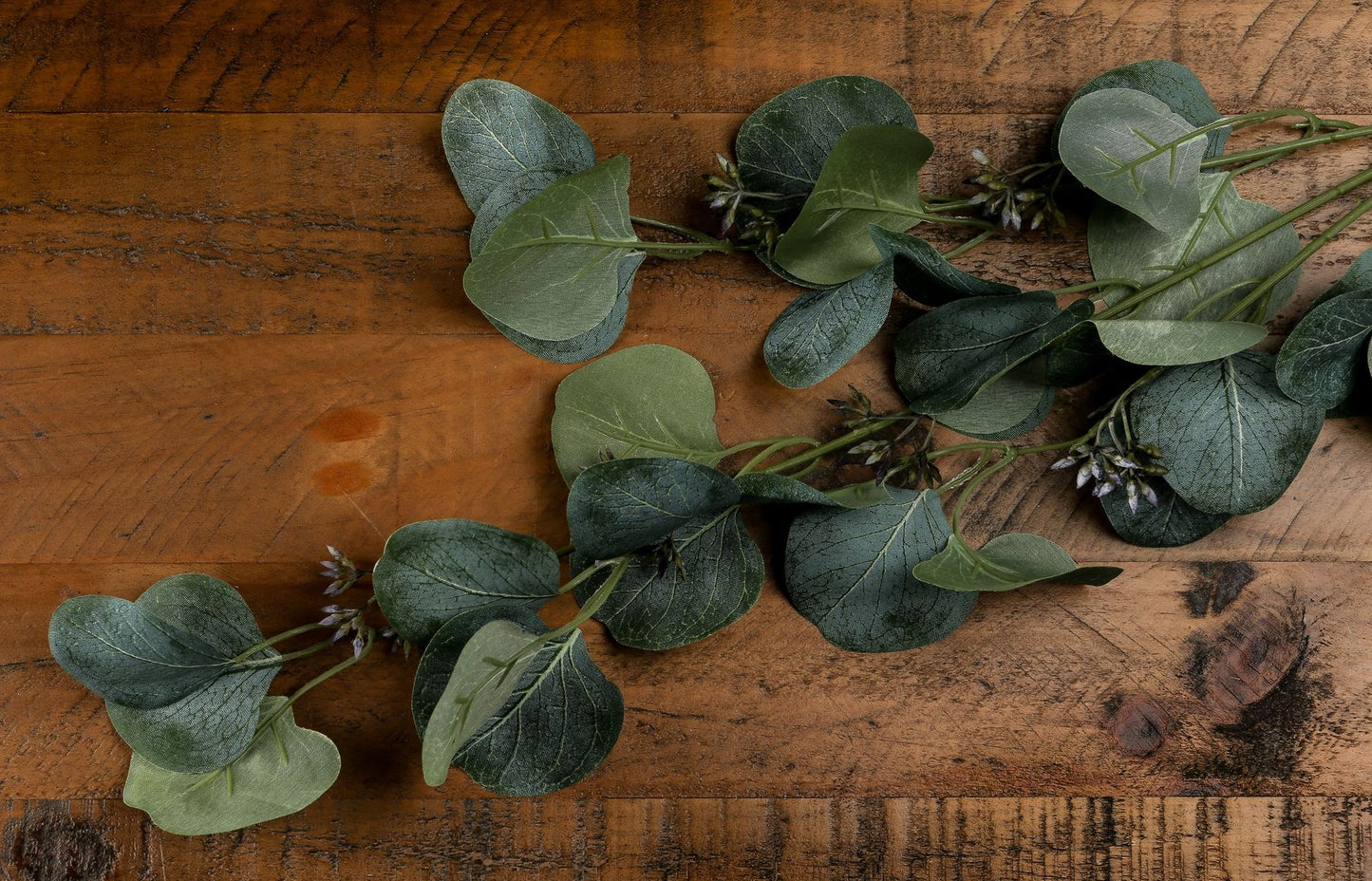 Realistic green eucalyptus stem spray arranged on a wooden surface, featuring lush leaves and subtle floral accents, perfect for decor.