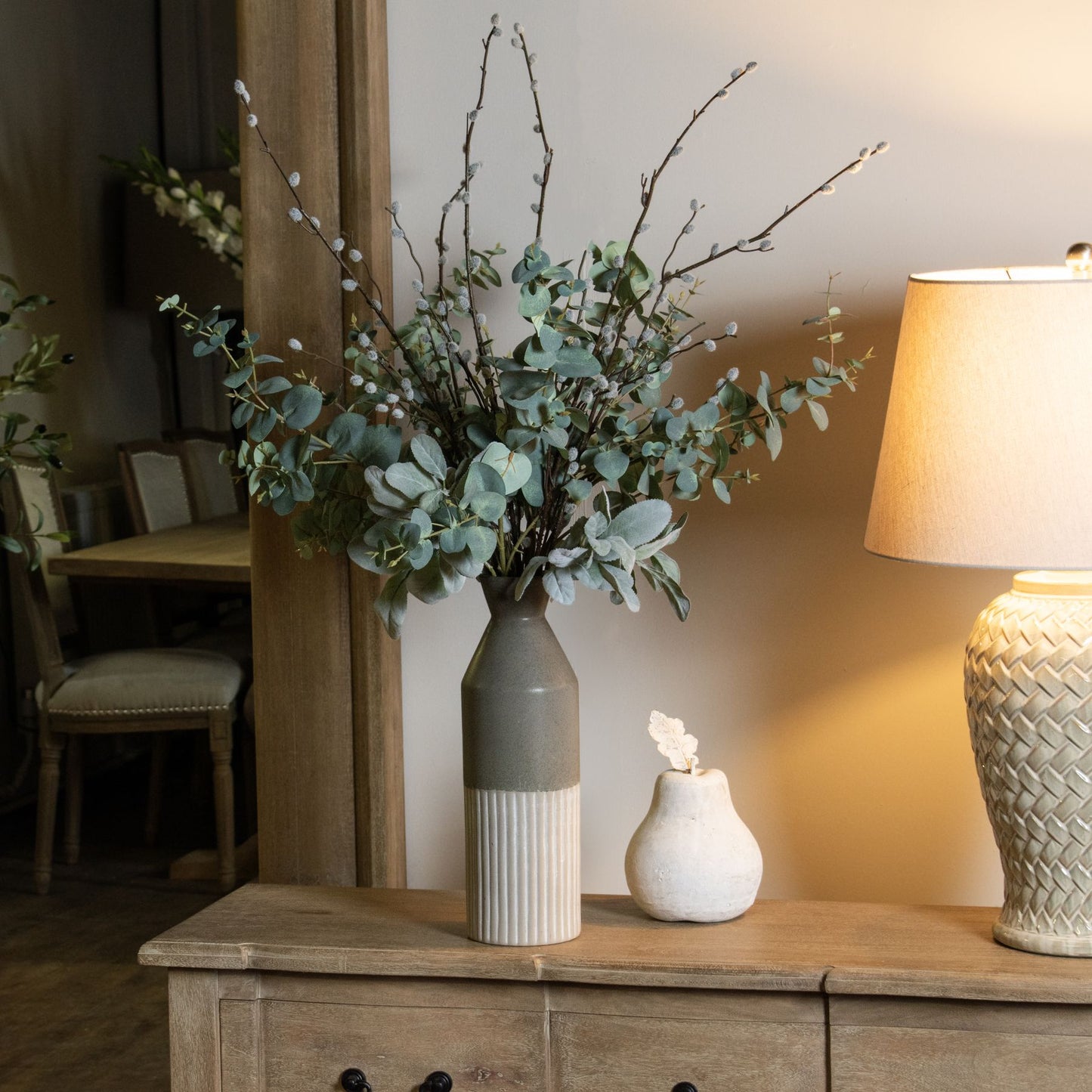 Tall, grey ceramic vase with a smooth curved top and ribbed base, adorned with lush greenery, set on a rustic wooden surface.