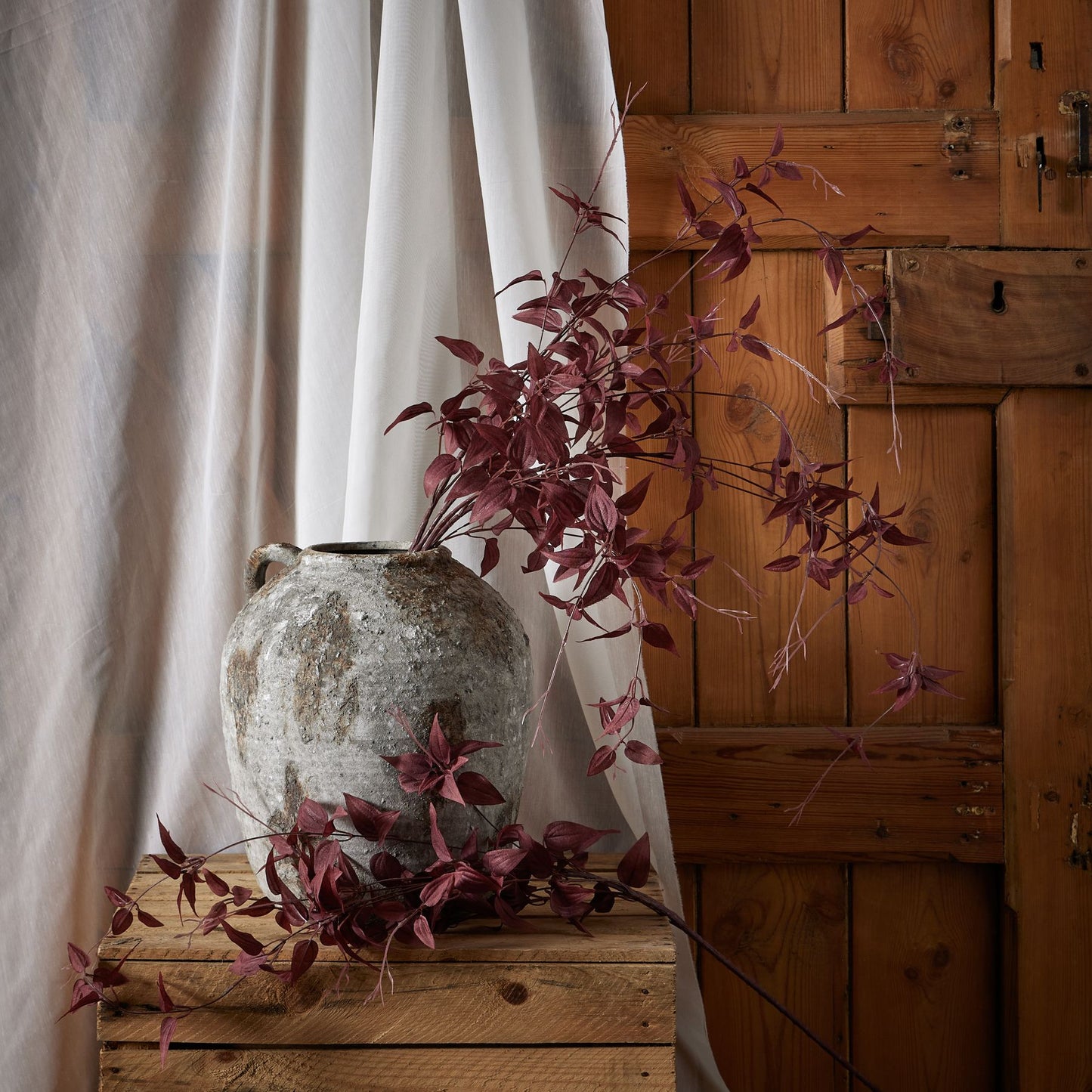 Artificial burgundy leaves elegantly arranged in a rustic pot, enhancing warm, autumnal home decor against a wooden backdrop.