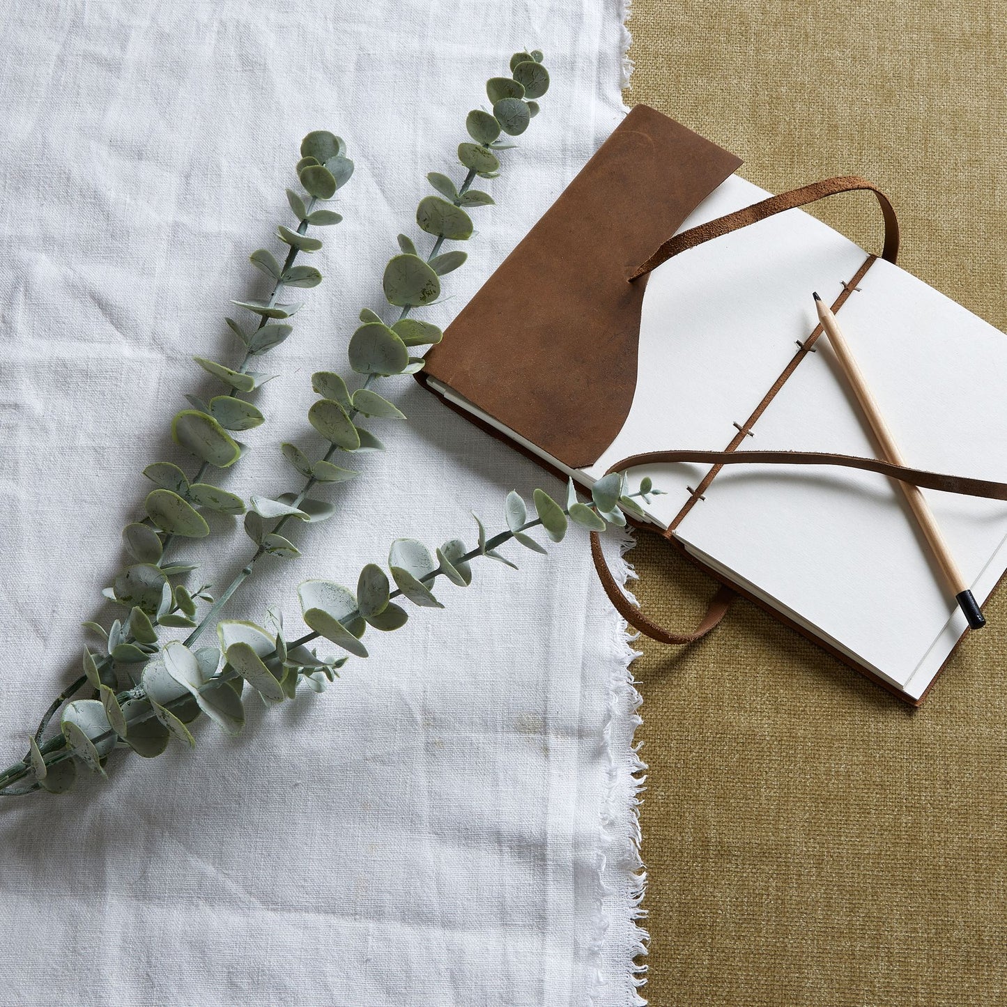 Gunnii Blue Eucalyptus Spray features silver-tinted leaves in a cool blue hue, artfully arranged with a brown notebook and pencil.