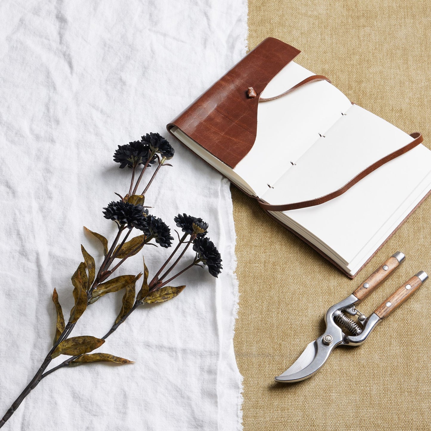 Elegant black chrysanthemums with richly textured petals, paired with rustic foliage, alongside a leather-bound notebook and garden shears.