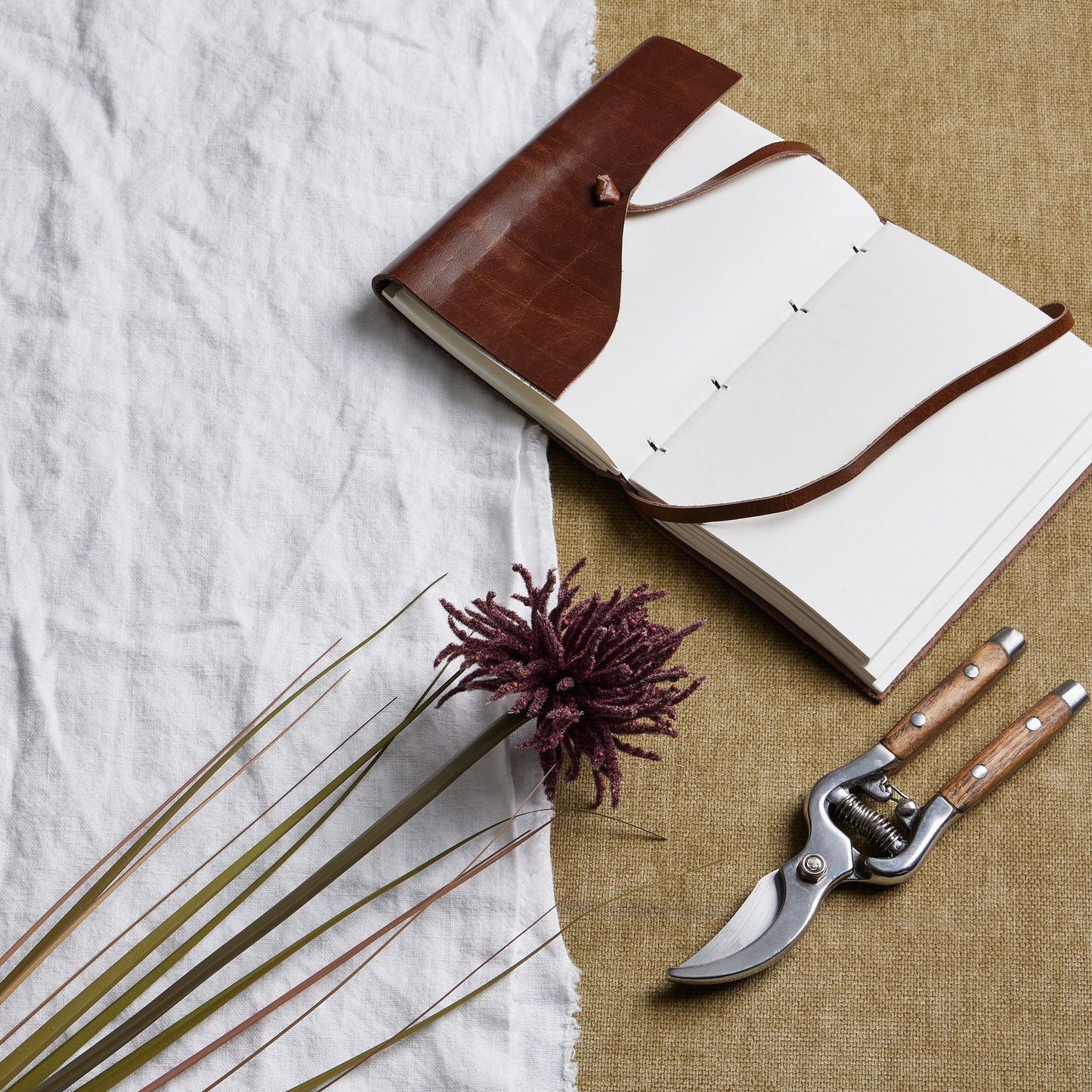 Burgundy Aster Spider Chrysanthemum stem with textured, layered petals, set beside a brown notebook and pruning shears on a neutral backdrop.