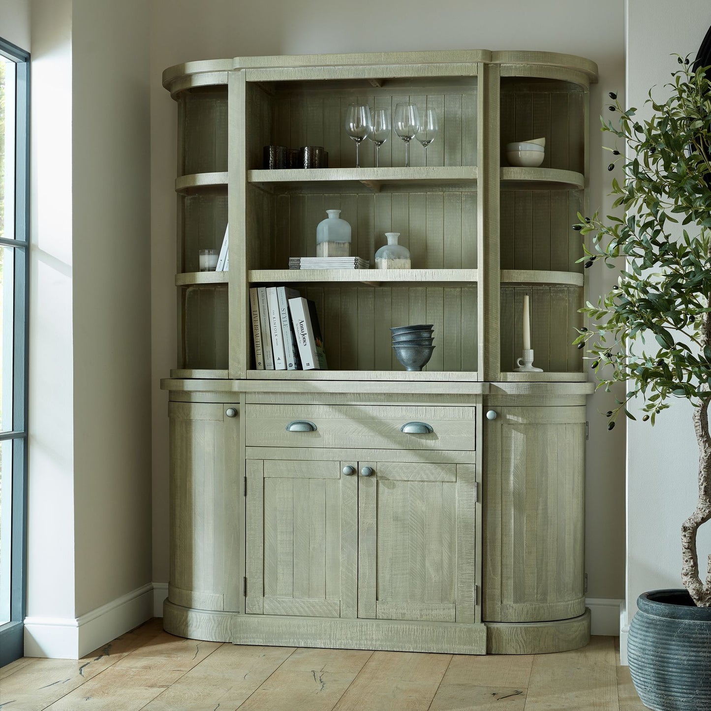 Curved, weathered red storage cabinet with shelves, glassware, and decorative items, adding modern elegance to any space.