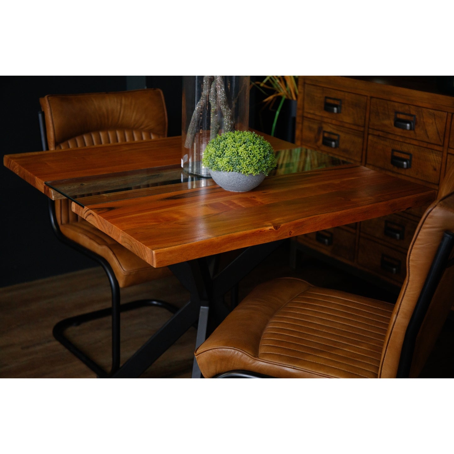 Live edge square dining table featuring rich wood grain, a glass river accent, and a sleek black metal base, paired with brown leather chairs.