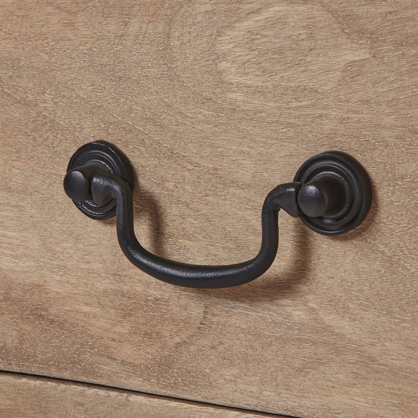 Close-up of a handcrafted drawer handle featuring black ironwork against a washed, bleached wood surface. Elegant and refined.