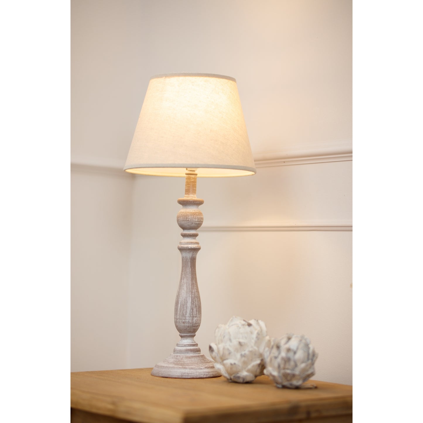 Dunum column table lamp features a rustic white base and soft linen shade, casting warm light beside elegant decor.