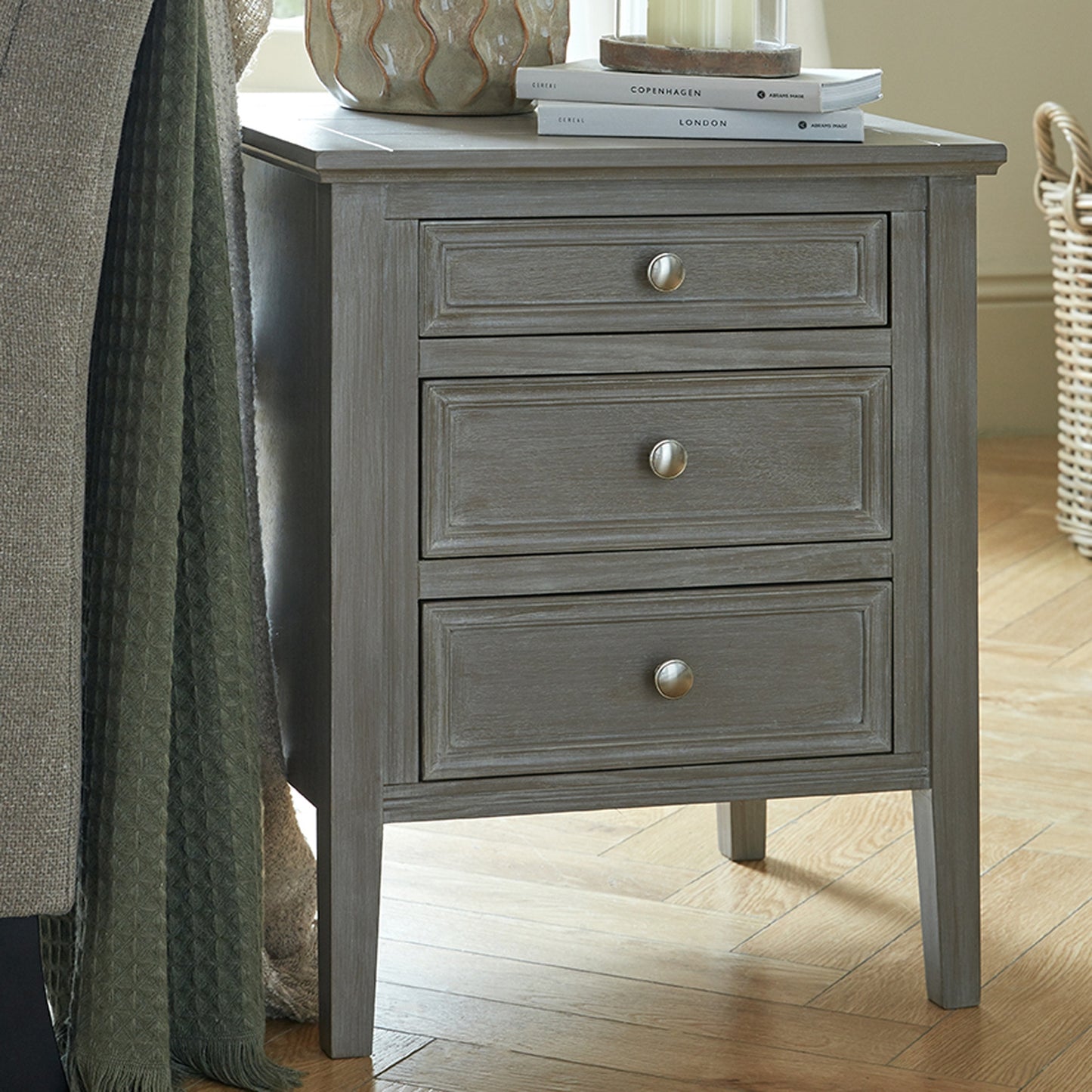 Sophisticated three-drawer bedside table in a distressed grey finish, featuring elegant handles and a refined design.