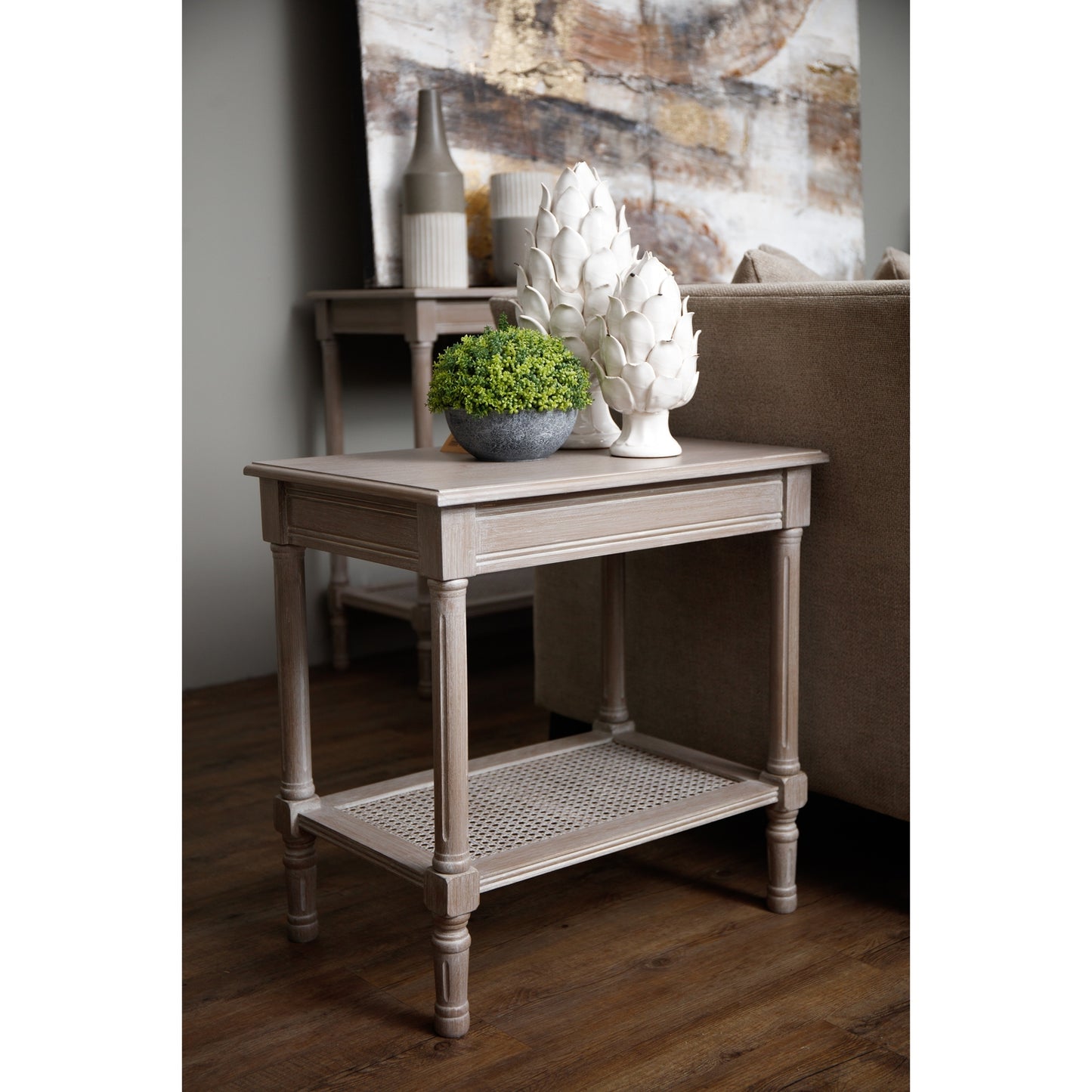Sleek side table in light gray with rattan detailing, adorned with a potted plant and decorative white sculptures, enhancing a tranquil living space.