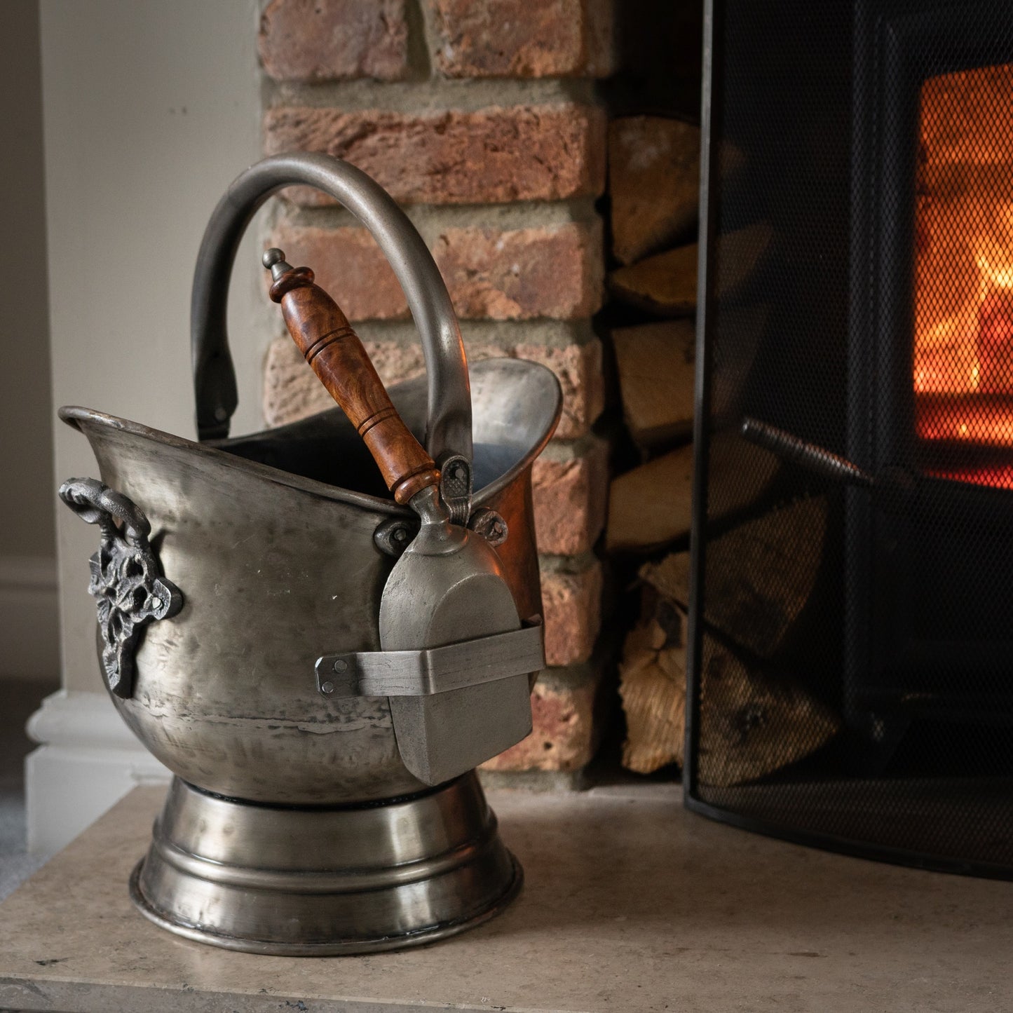 Antique pewter coal bucket with a wooden handle and matching shovel, featuring intricate floral embossing and a weathered finish.