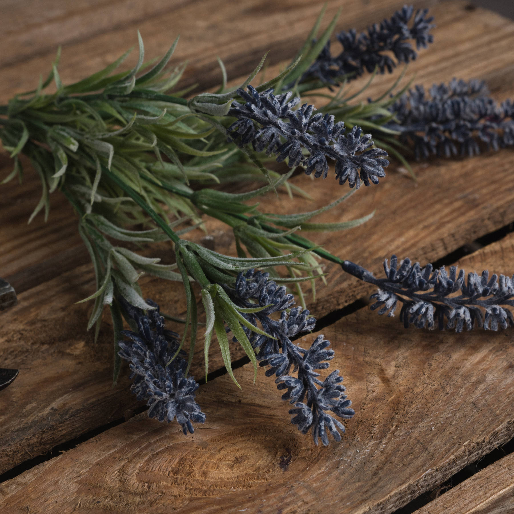 Small lavender spray with realistic purple blooms and green foliage resting on rustic wooden surface, adding elegant, maintenance-free beauty.