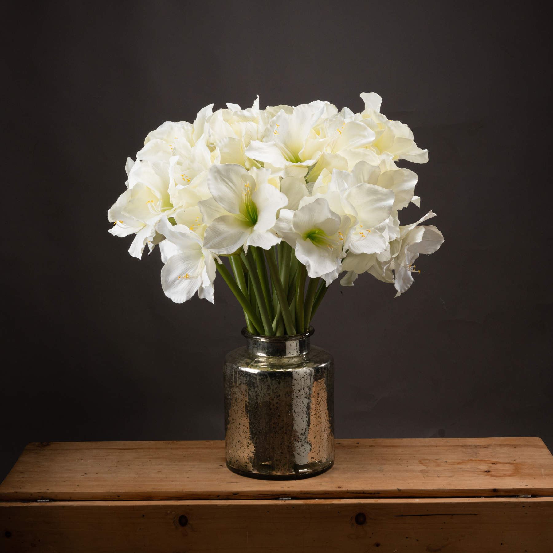 Tall artificial white amaryllis flowers in a textured silver vase, featuring two open blooms and a closed bud, enhance elegant decor.