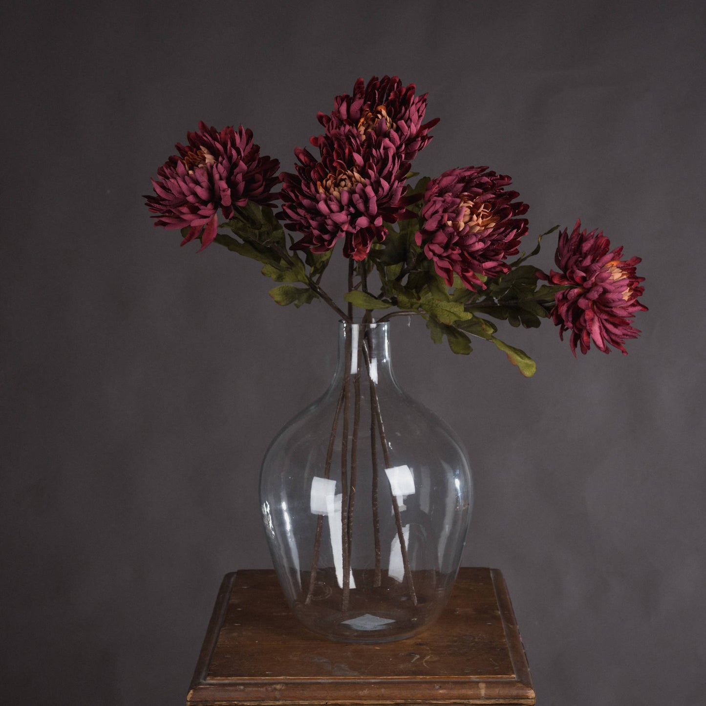 Sophisticated artificial spider chrysanthemums in rich red hues, displayed in a glass vase, enhance autumn decor with elegance.