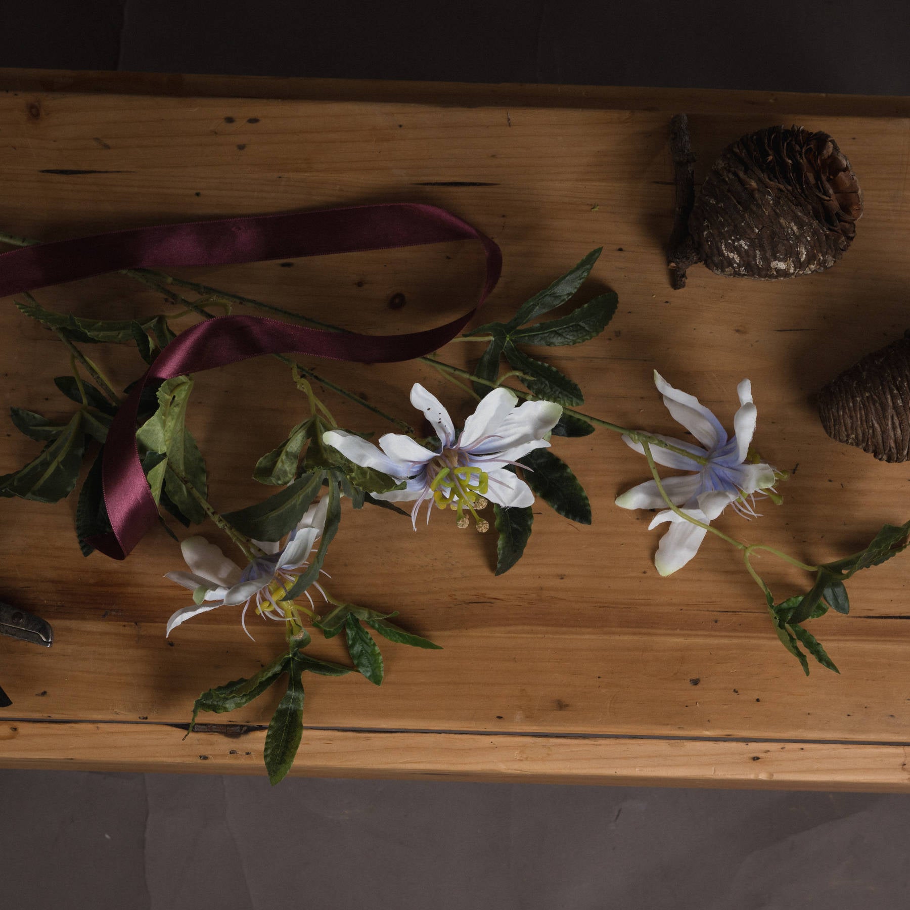 Liflike Passion Flower Spray featuring white petals with delicate purple accents and lush green leaves on a wooden surface.