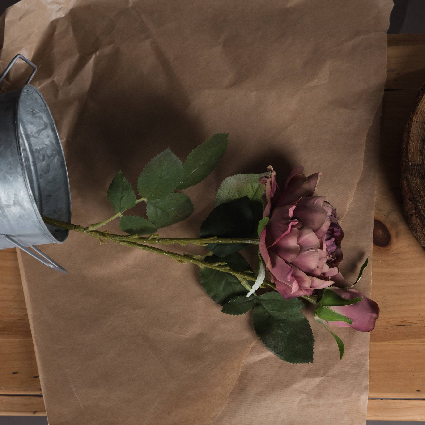 Dusty pink spray rose peony with realistic blooms and lush green leaves, set against brown kraft paper and wood.