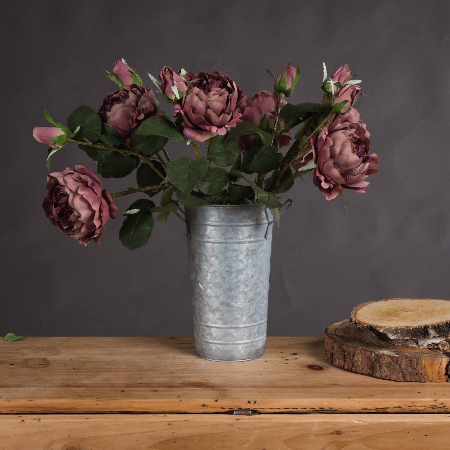 Dusty pink spray rose peonies in a galvanized metal vase, set against a dark background, enhance rustic elegance.