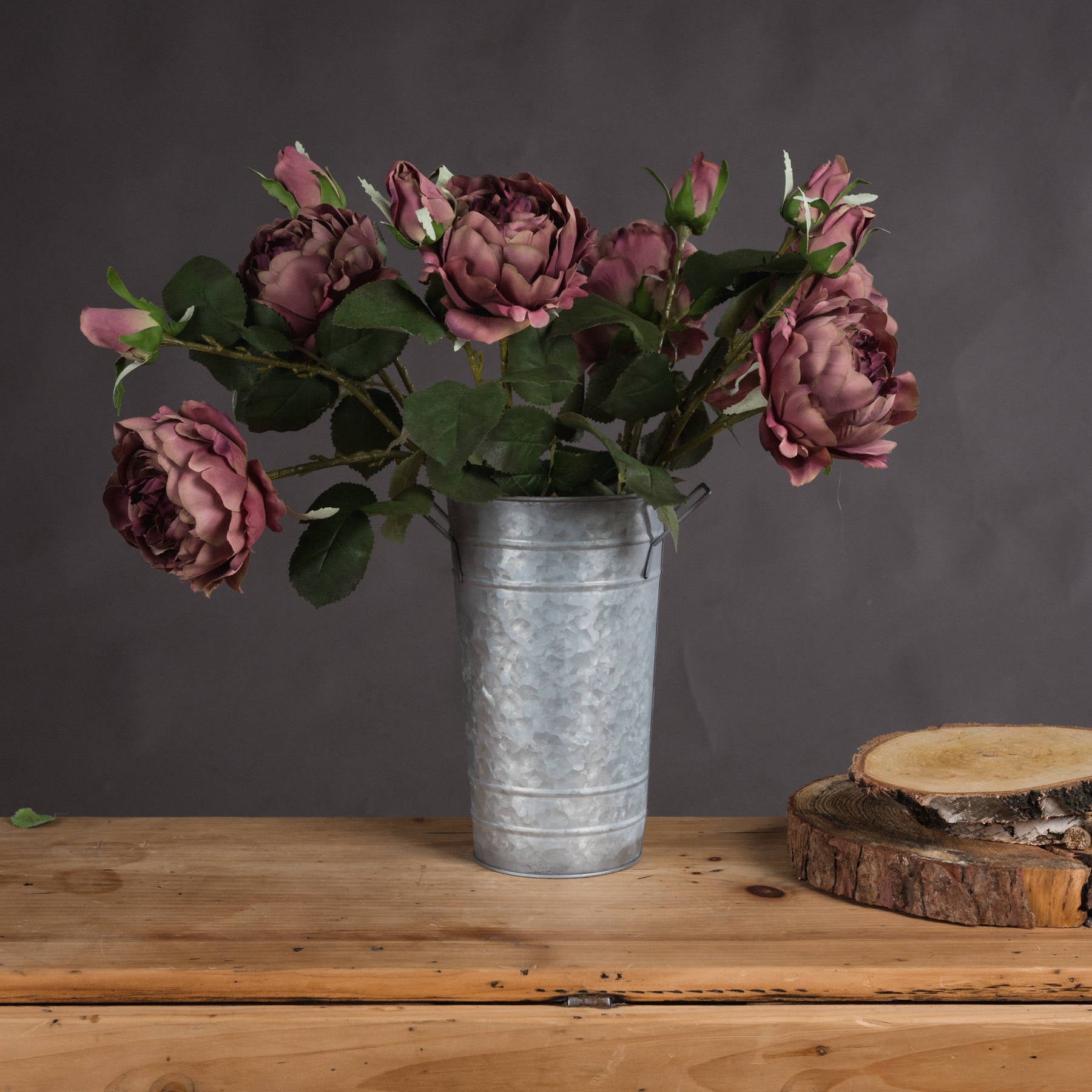 Dusty pink spray rose peonies in a galvanized metal vase, set against a dark background, enhance rustic elegance.