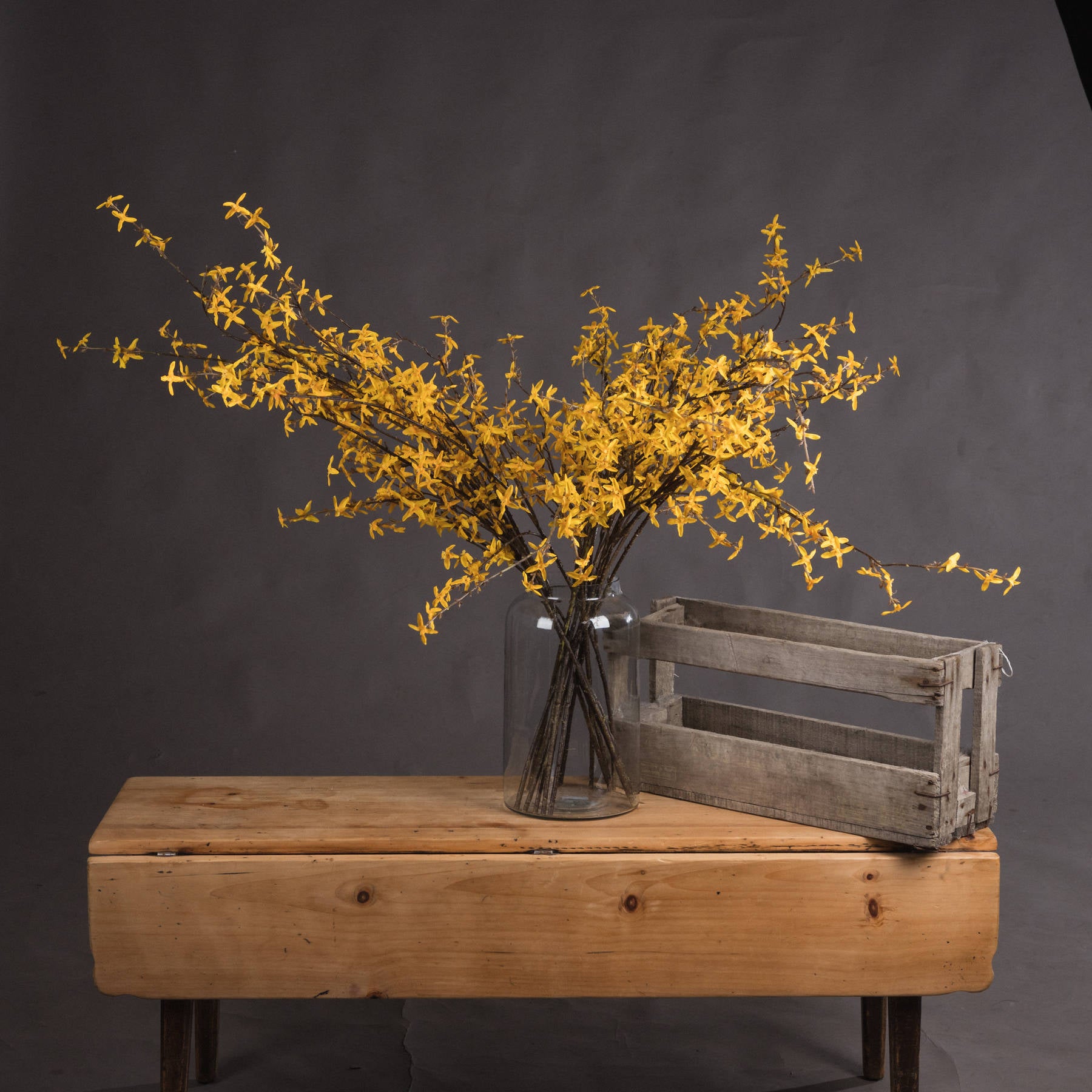 Vibrant yellow forsythia stems in a glass vase on a wooden table, radiating warmth and elegance for any decor.