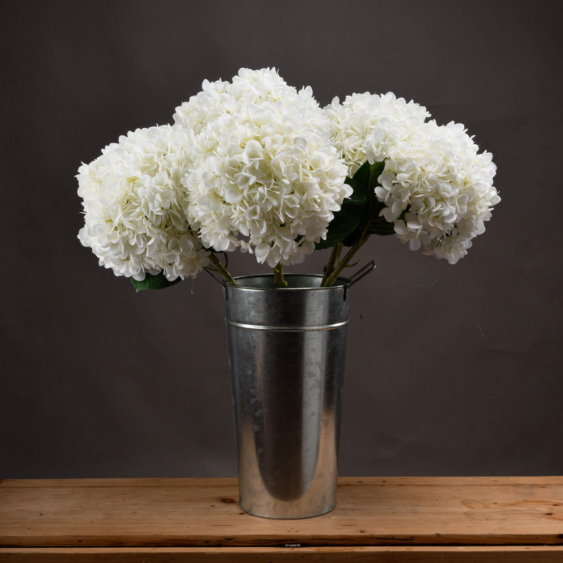 Oversized white hydrangea in a silver metal vase, showcasing full-bodied blooms against a neutral background. Perfect for elegant decor.