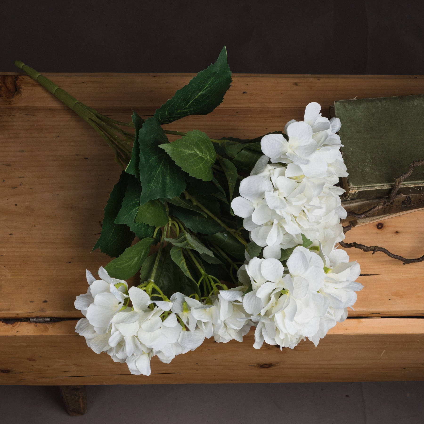 Lifelike white hydrangea bouquet with lush green leaves, perfect for elegant home decor, resting on a wooden surface.