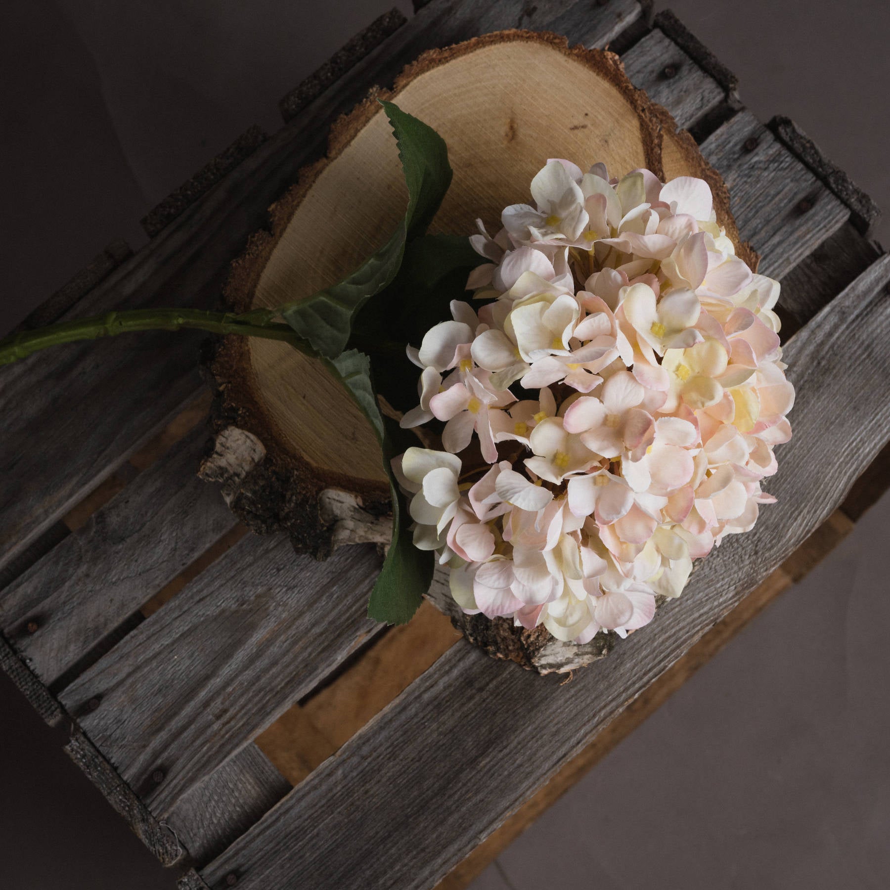 Artificial white hydrangea stem with subtle blush petals, resting on a wooden surface, perfect for autumn decor.