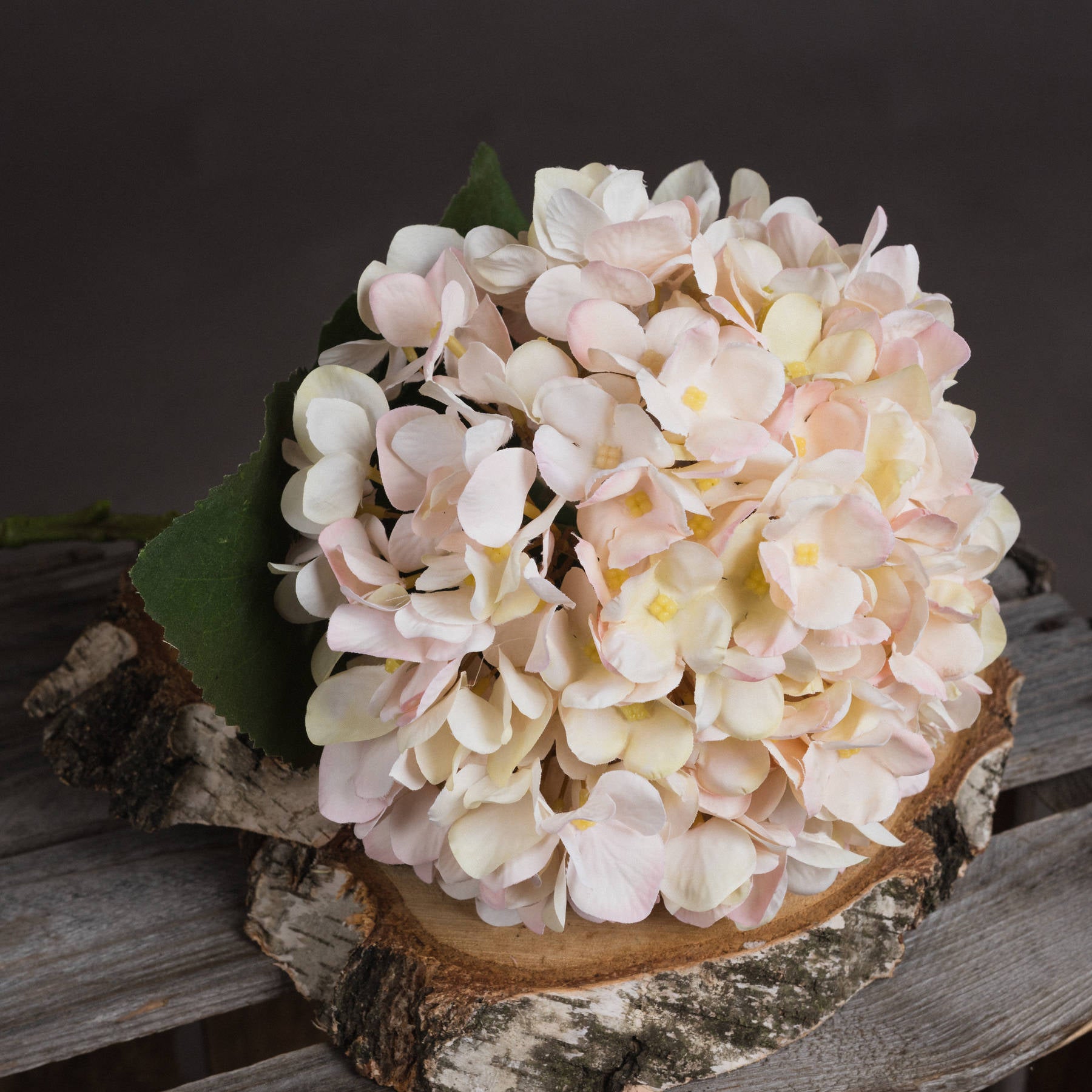 White hydrangea stem with hand-painted petals featuring soft blush undertones, set on a natural wood surface for an elegant display.