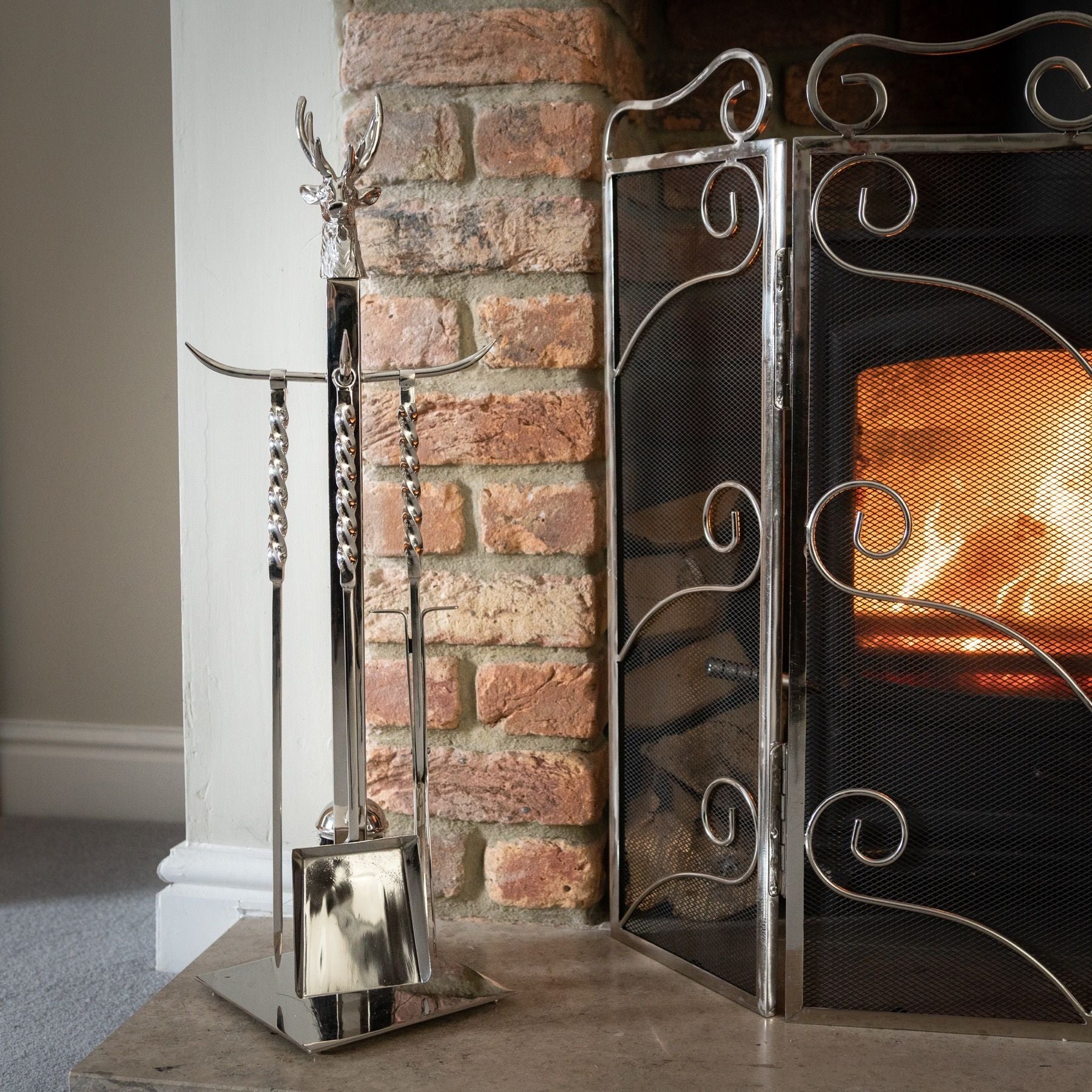 Handcrafted companion set featuring a polished nickel stag head and elegant tools, standing at 67cm, beside a cozy fireplace.
