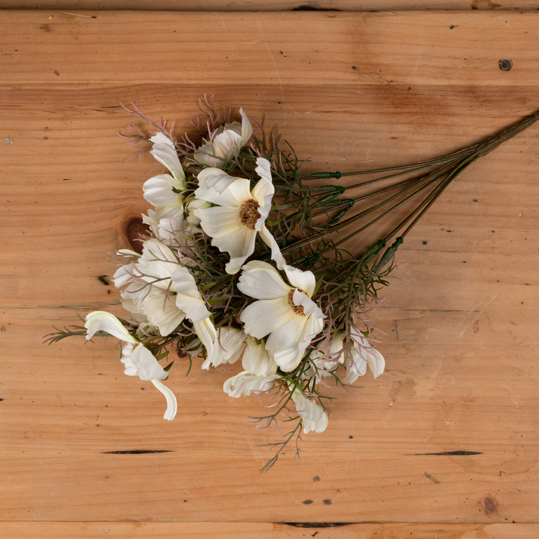 Cream cosmos spray featuring soft cream petals and delicate green foliage, arranged elegantly on a wooden surface.
